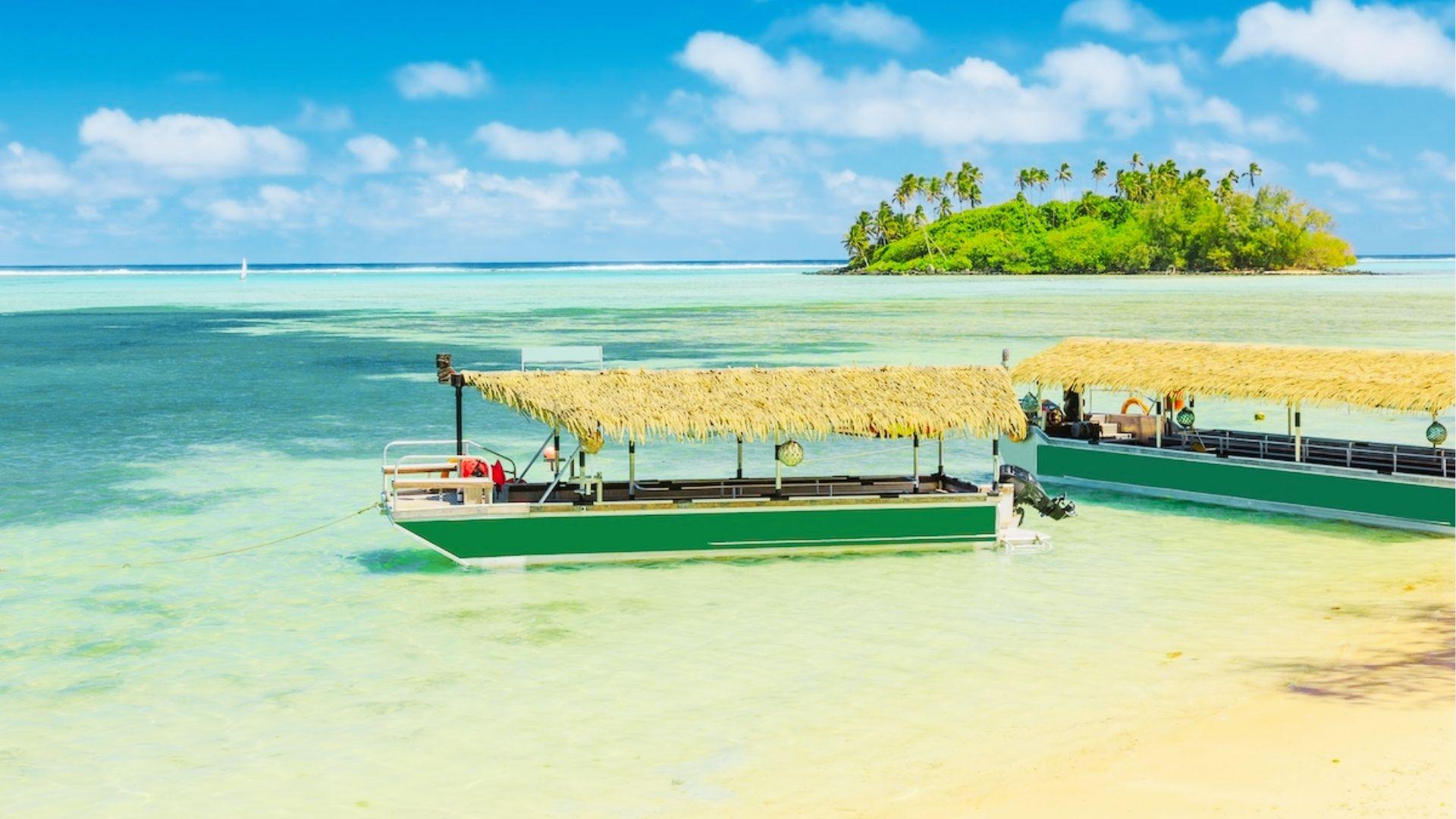 Green thatched roof boats float on shallow turquoise water near palm covered island under blue