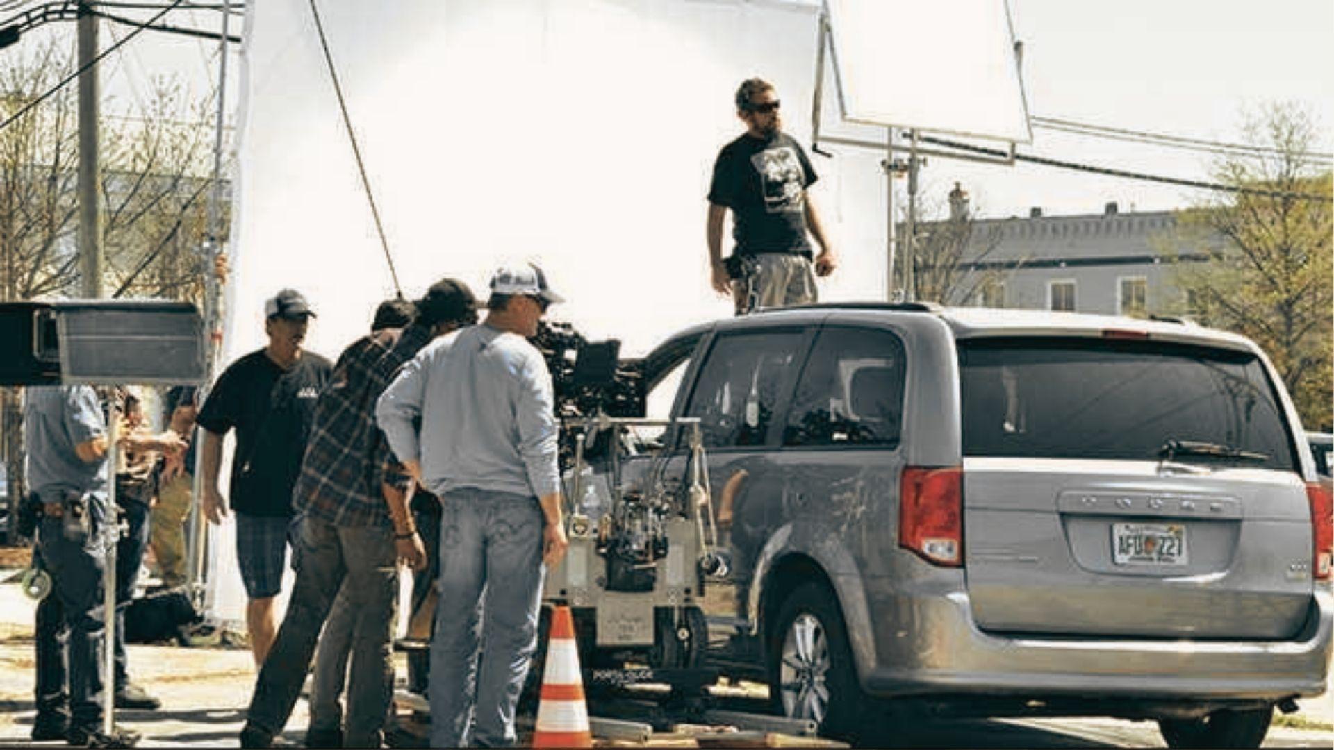 Film crew sets up a car rig with camera and lighting scrims on a city street.