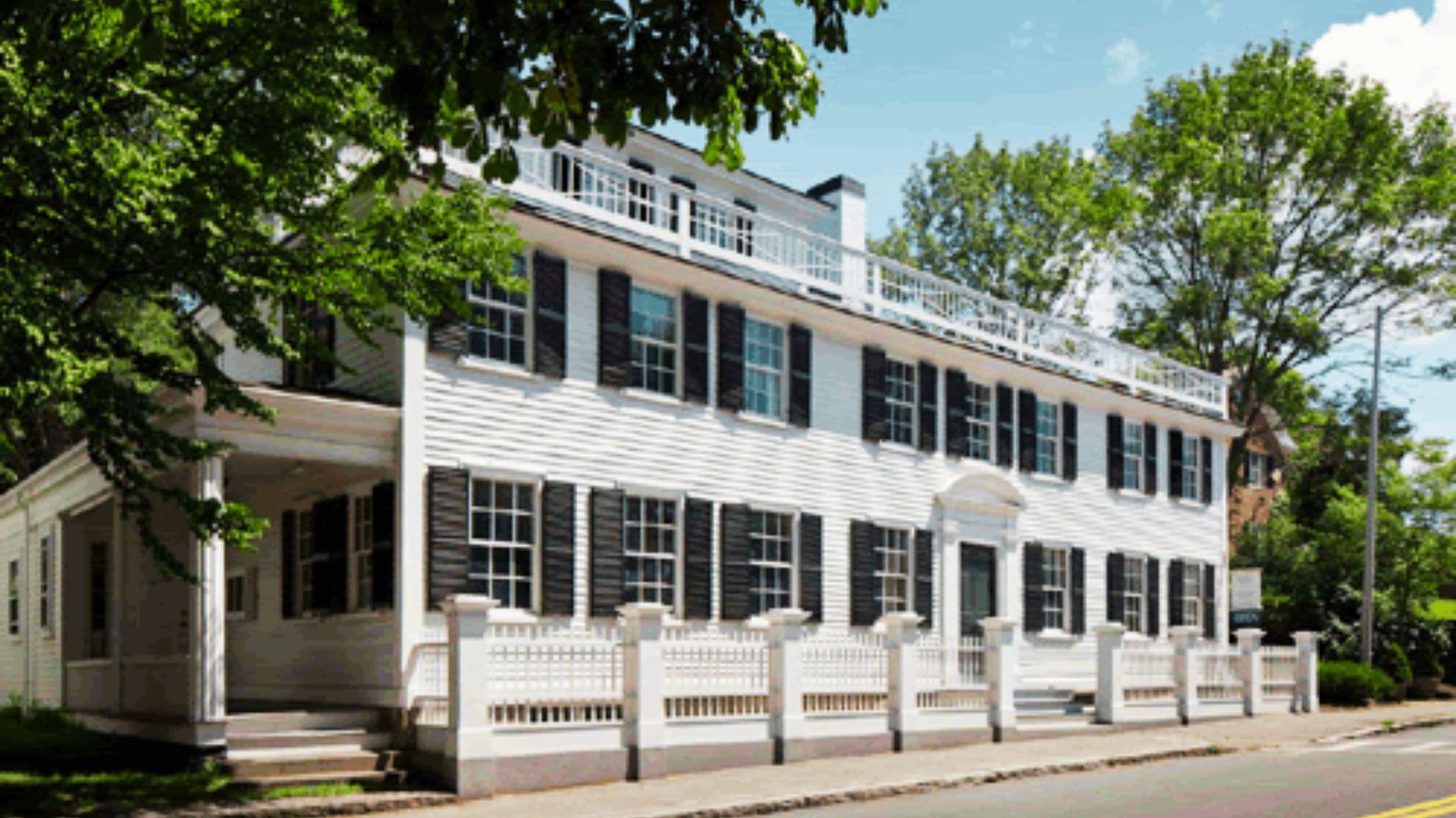 Trask House Museum with black shutters and a white picket fence lines a quiet street in Manchester-by-the-Sea.