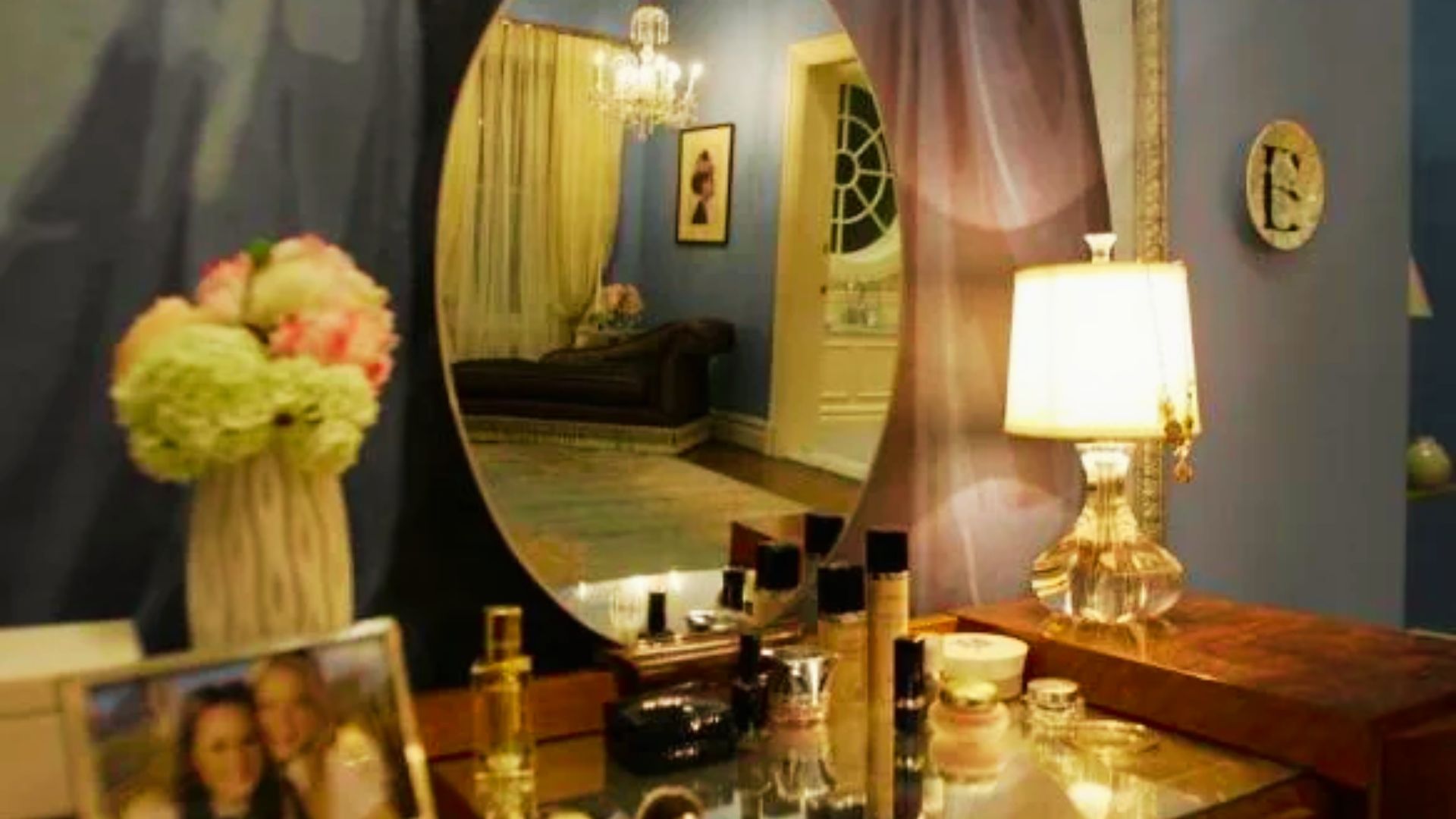 Vanity area in Blair’s bedroom featuring an oval mirror, perfume bottles, and a lamp on a mirrored tabletop.