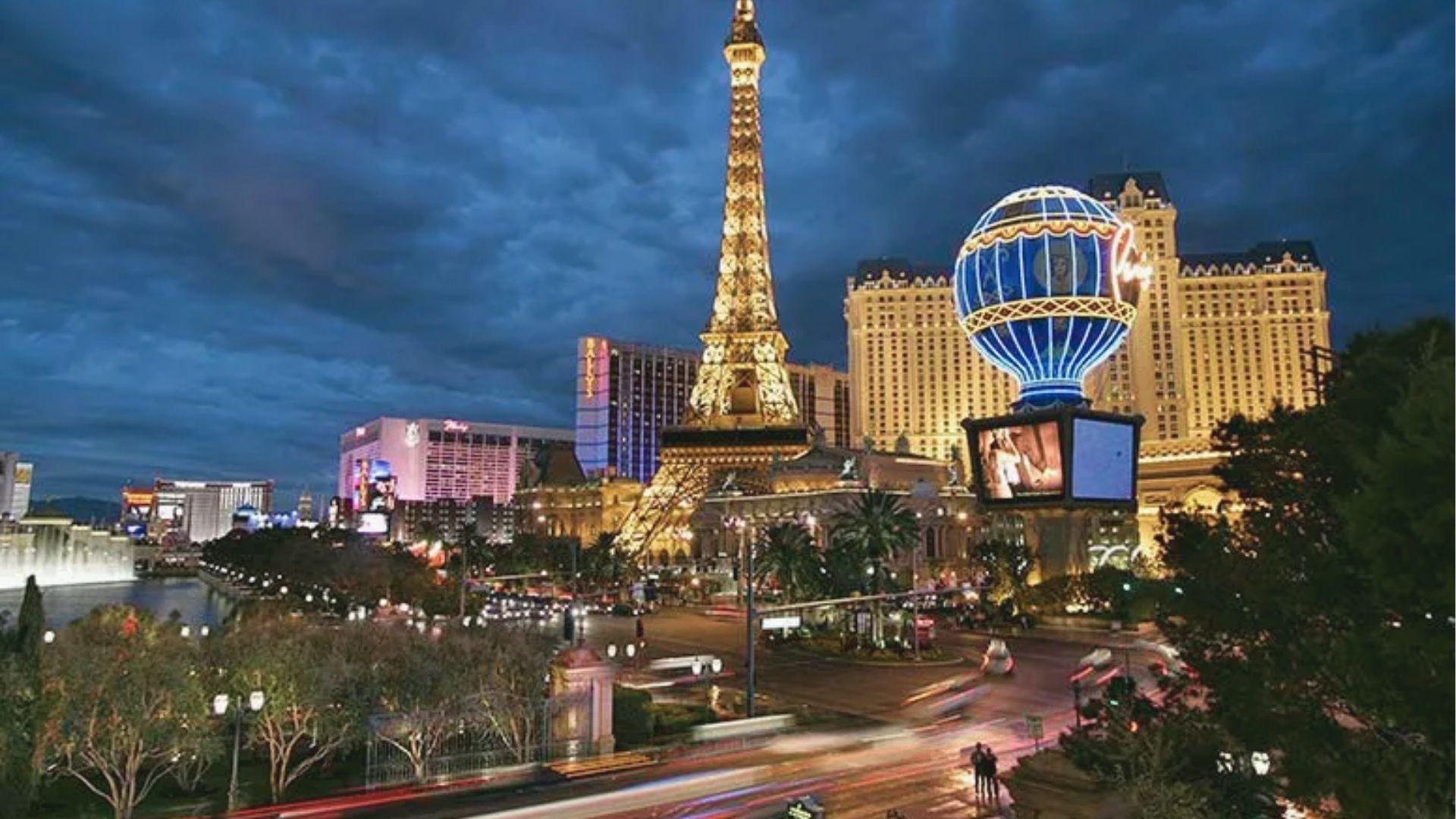 Glowing Eiffel Tower replica and Paris Hotel balloon light up the Las Vegas Strip as traffic blurs below.