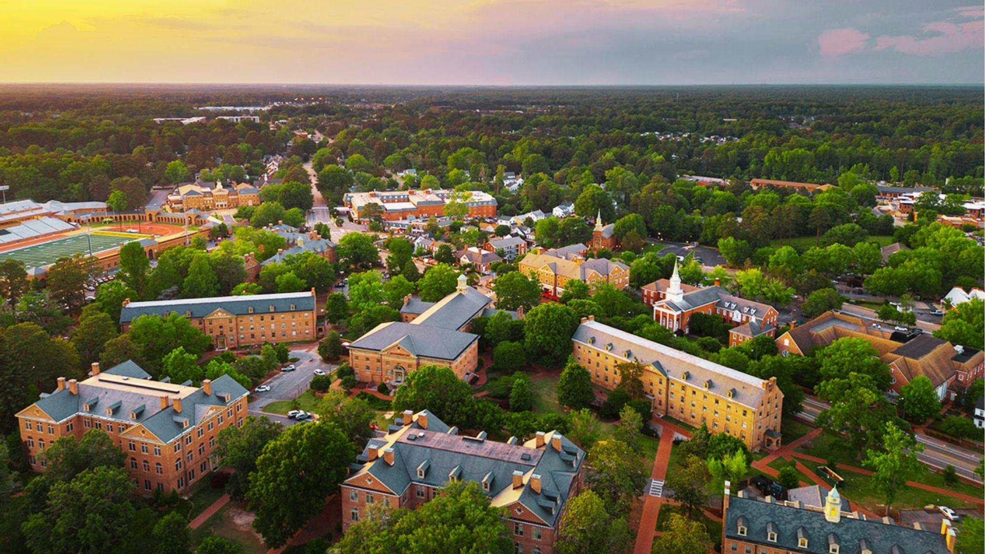 Aerial view of historic brick college campus with green trees, pathways, and sunset golden light