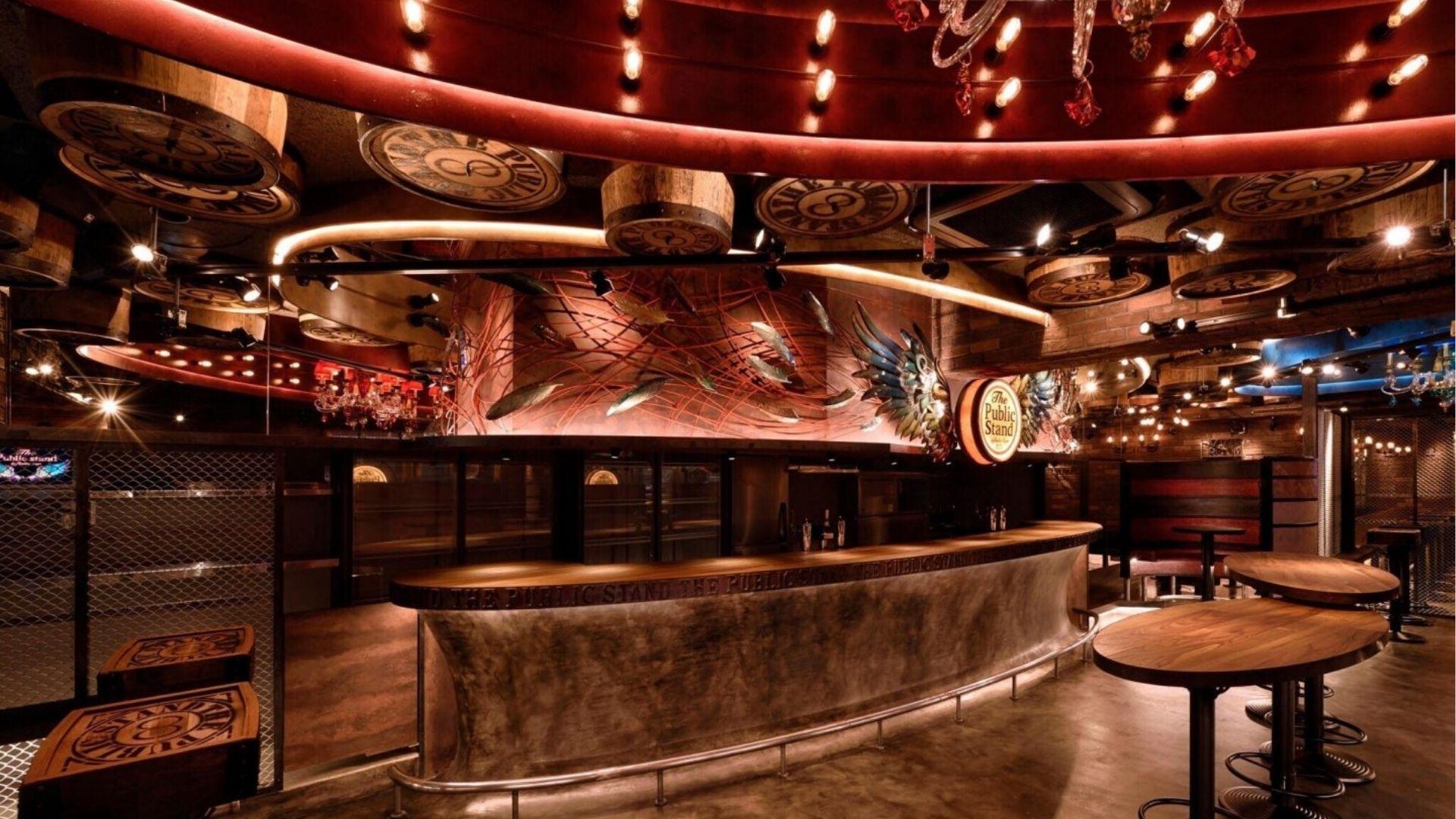 Dimly lit bar interior with barrel decor, wood tables, and industrial steampunk design.