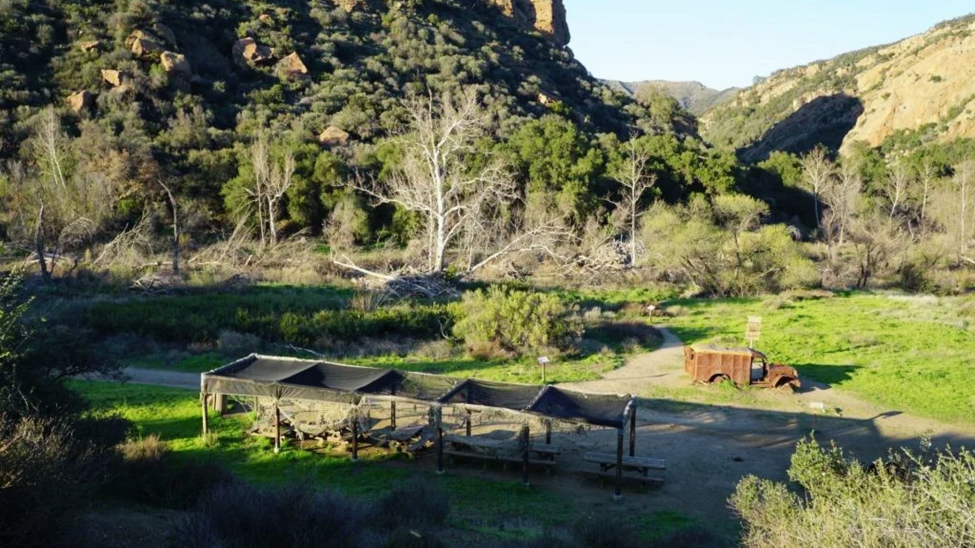 Green valley and picnic shelters at Malibu Creek State Park, with a rusted truck nearby.