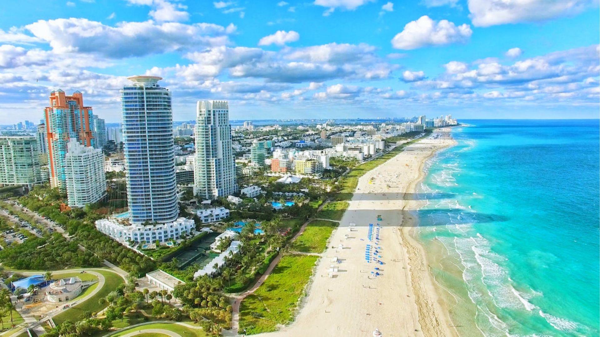 High-rise hotels and turquoise water stretch along Miami Beach’s white sand under a bright sky.