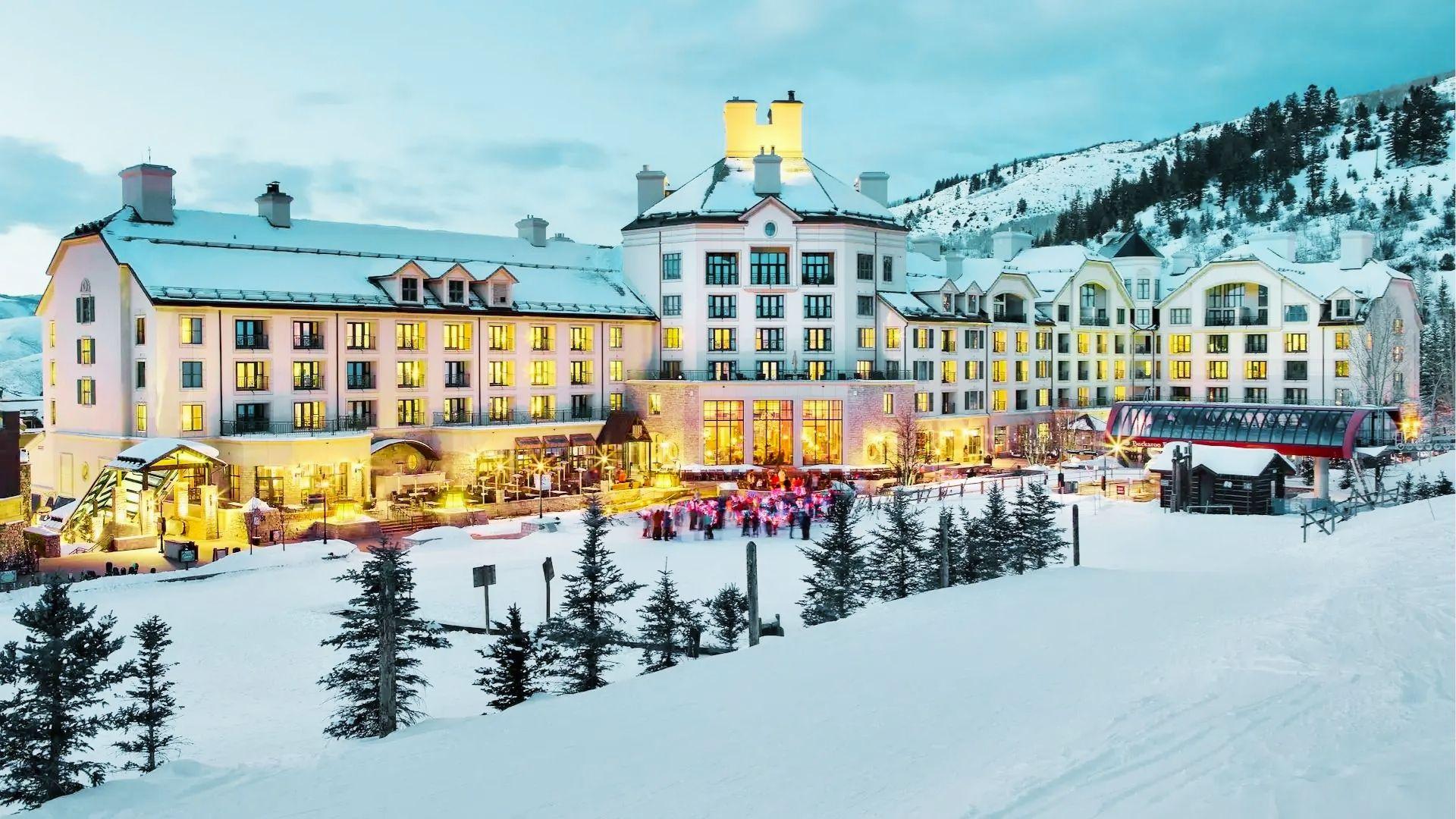 Luxury snow covered ski resort hotel glows at dusk with crowds gathering and gondola nearby