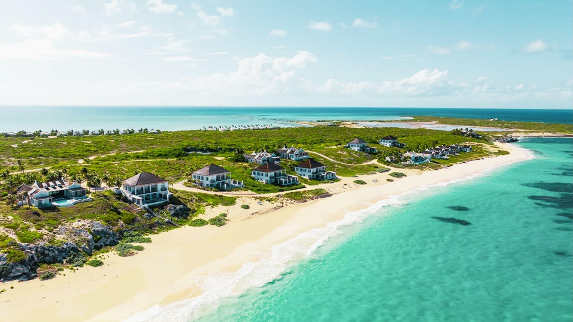 Luxury beachfront villas line white sand shore with turquoise water and green vegetation nearby island