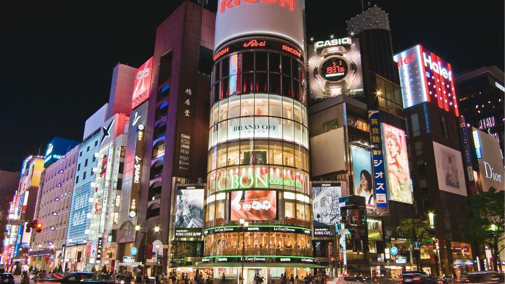 Neon-lit Ginza intersection at night with luxury brand storefronts like Dior and Haier towering over the street.