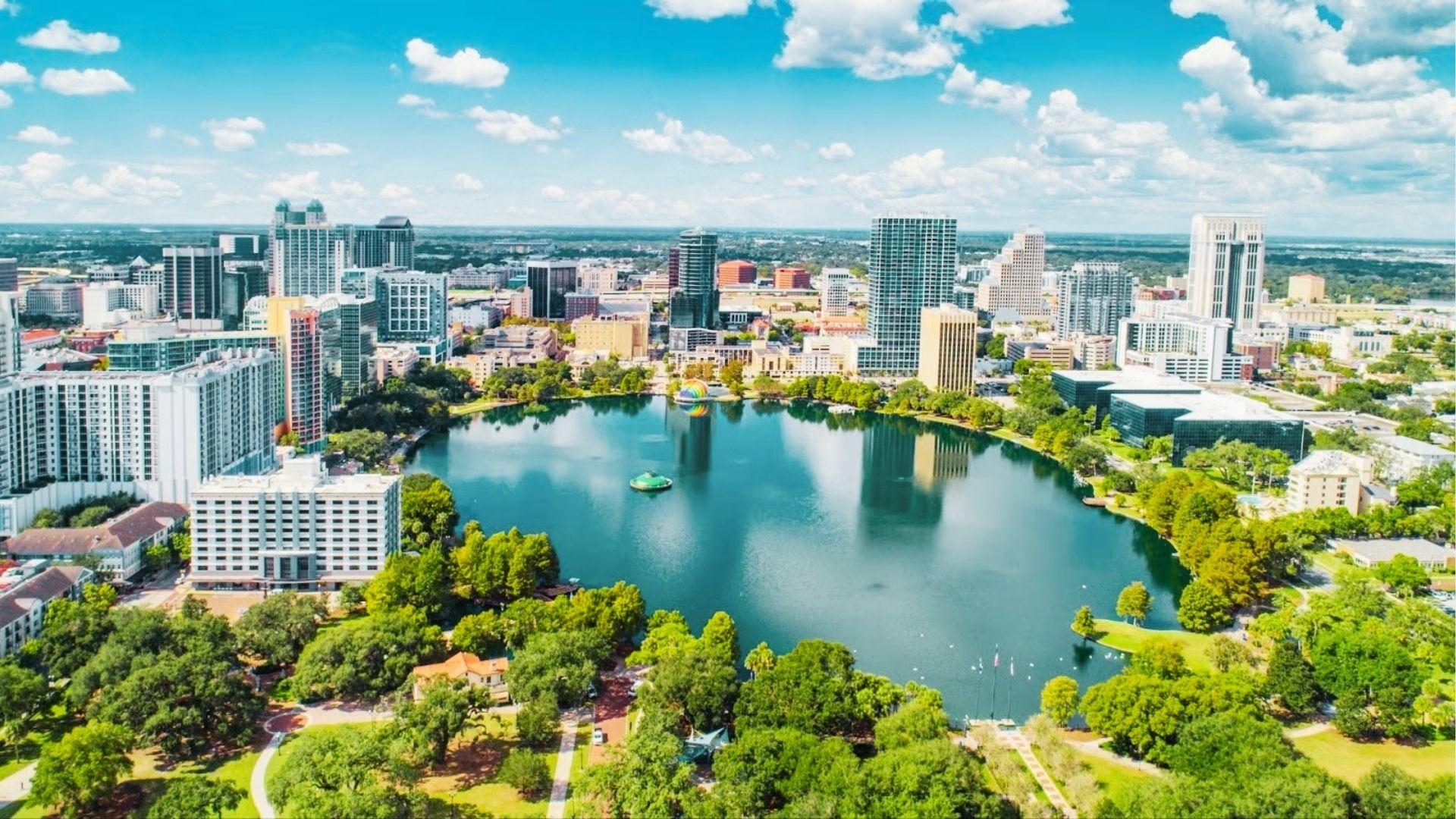 Aerial view of downtown skyline around blue lake with fountain, green parks, and skyscrapers under clouds