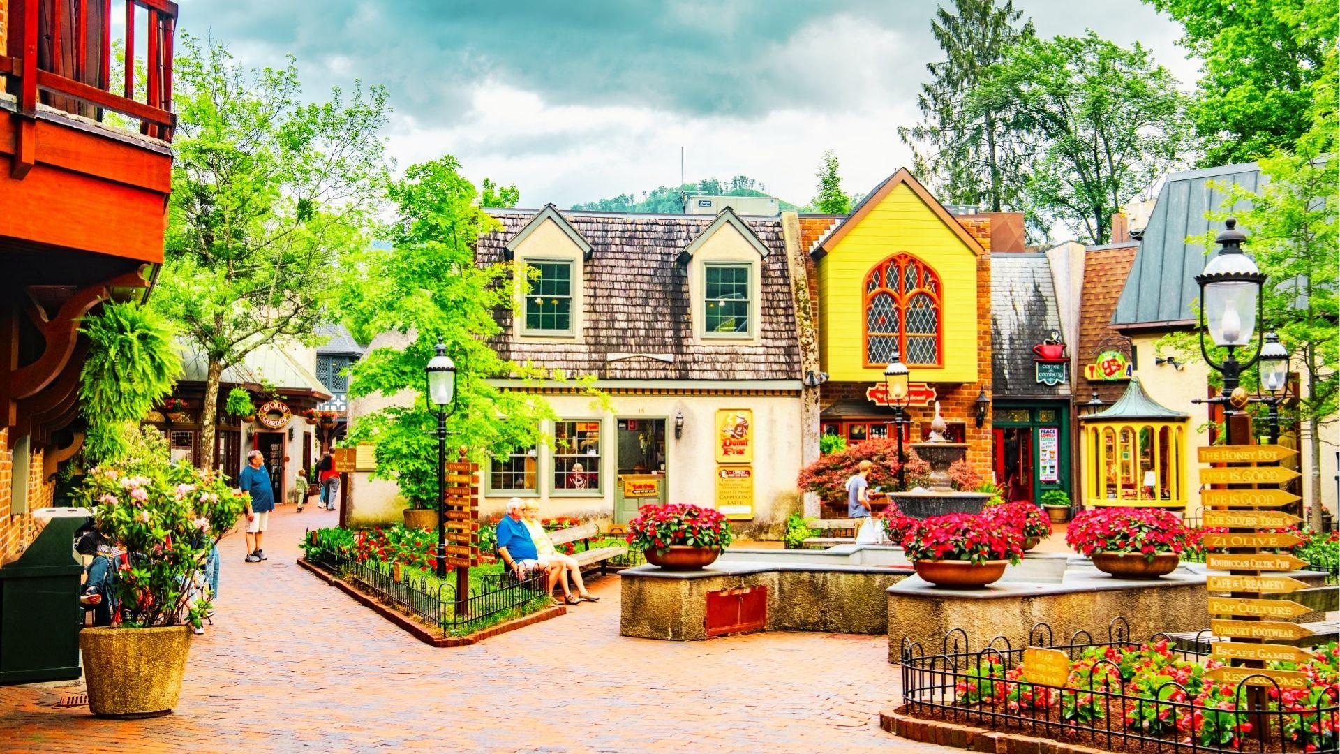Charming brick courtyard with colorful shops, red flowers, wooden signs, benches, and leafy green trees