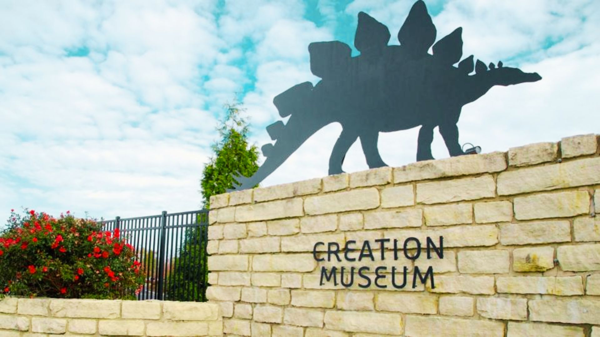 Stone entrance sign for the Creation Museum in Petersburg, Kentucky topped with a stegosaurus silhouette.