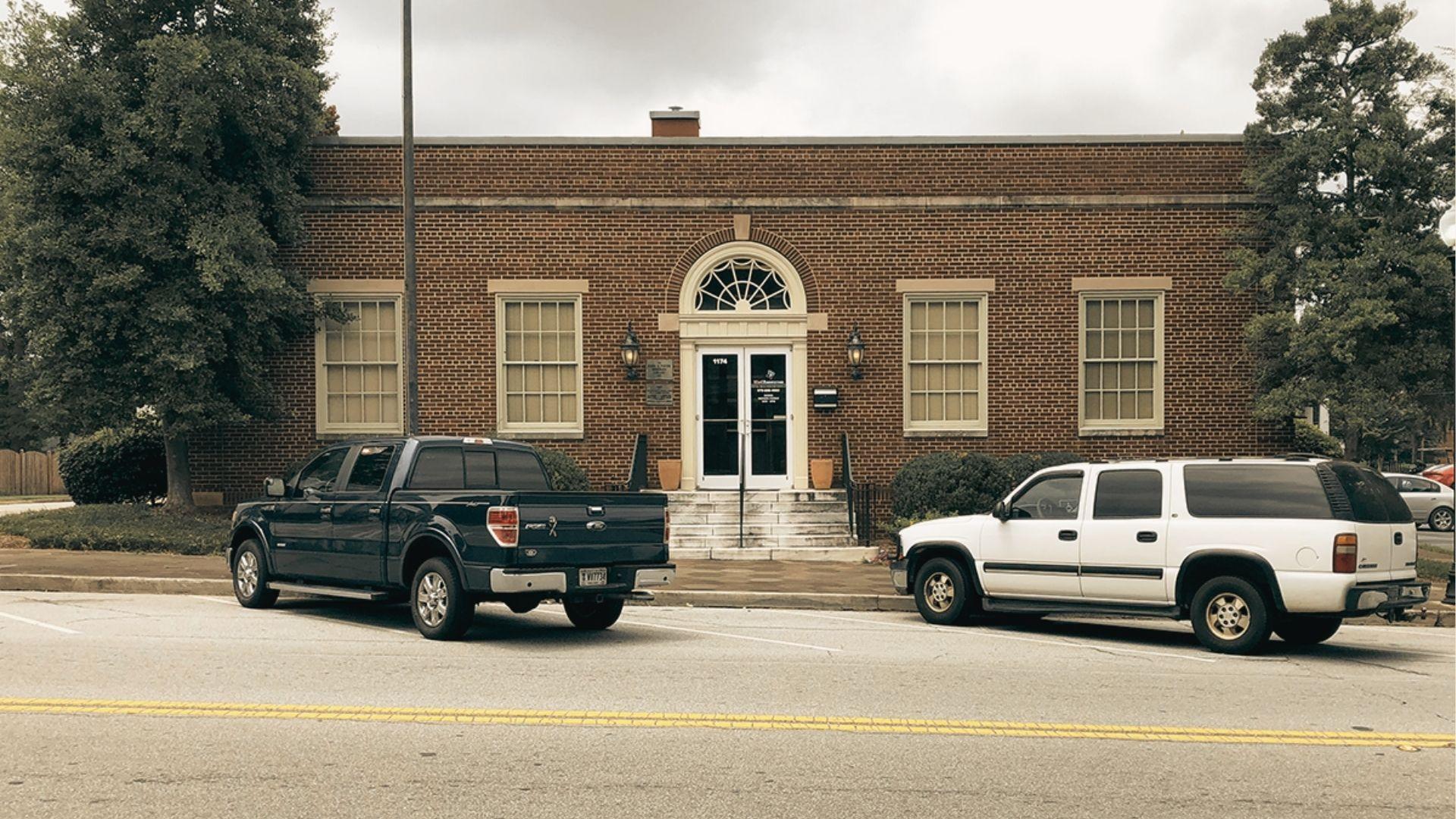 Front view of the same red brick municipal building with symmetrical windows and parked vehicles.