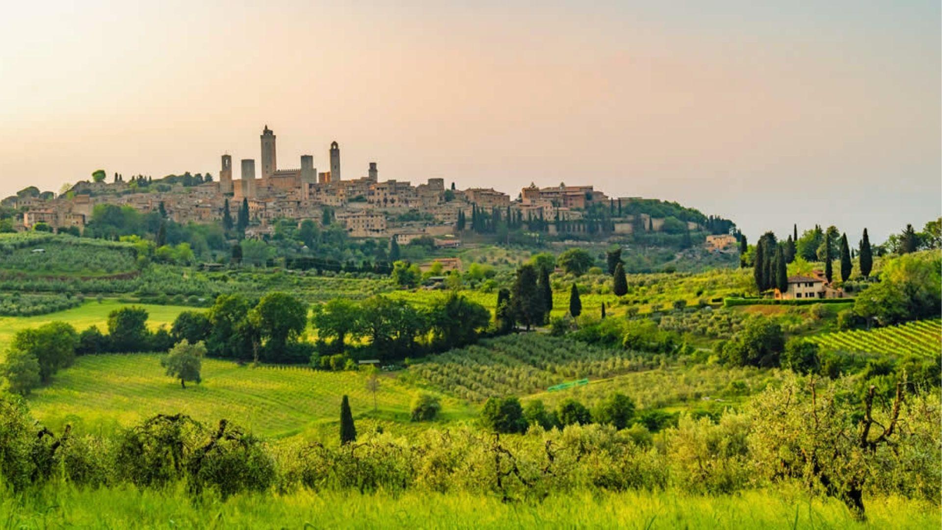 Rolling Tuscan hills glow in soft morning light, with San Gimignano’s medieval towers rising in the distance.