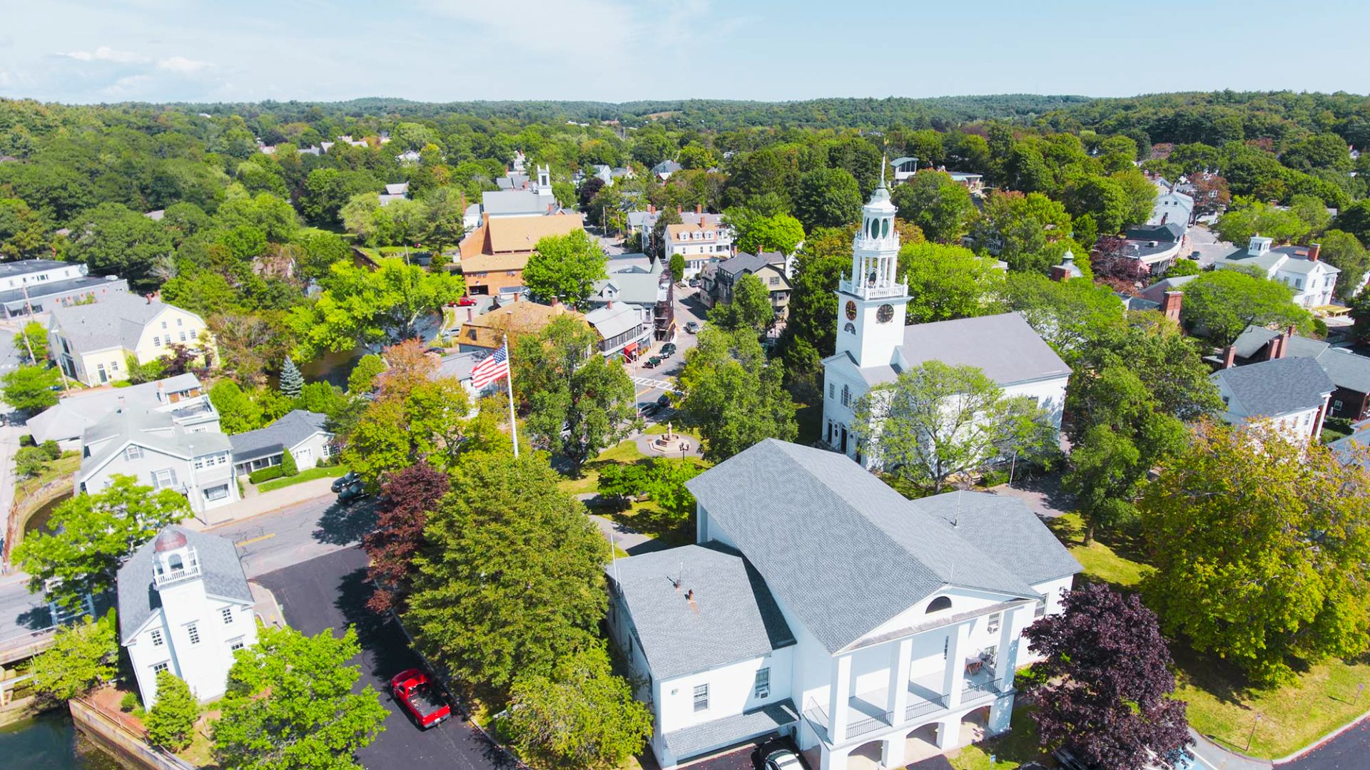 Aerial view of downtown Manchester-by-the-Sea shows white church steeples, historic buildings, and tree-lined streets.