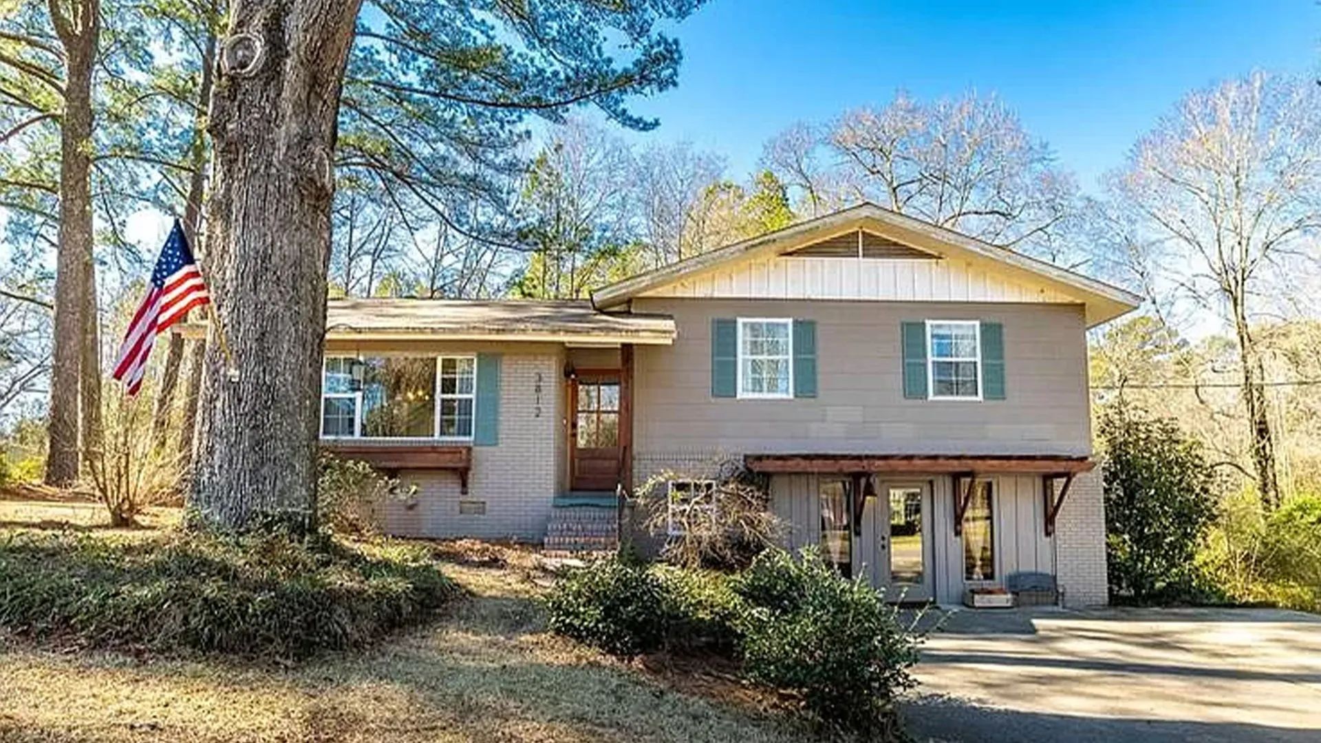Split-level suburban home in Laurel, Mississippi with blue shutters, a wood front door, and an American flag.