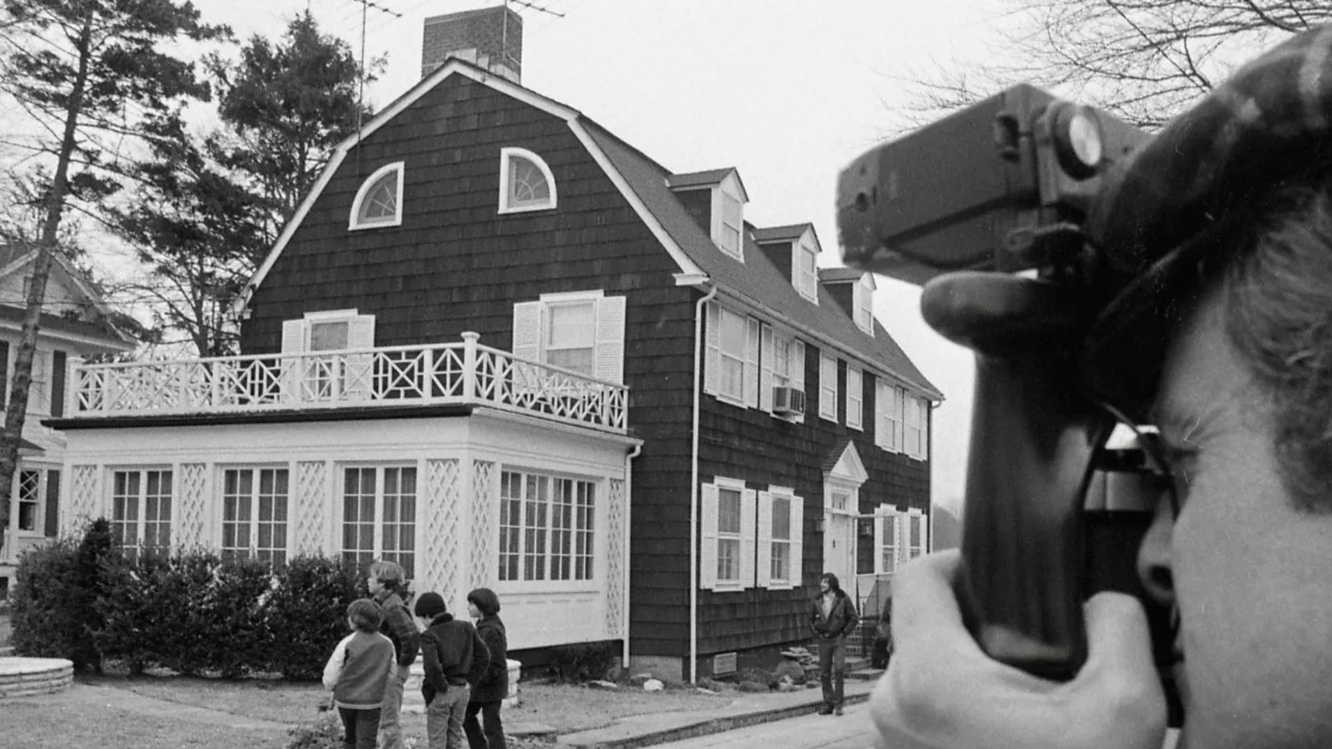 A man using a camera to capture the Amityville Horror House, known for its famous history