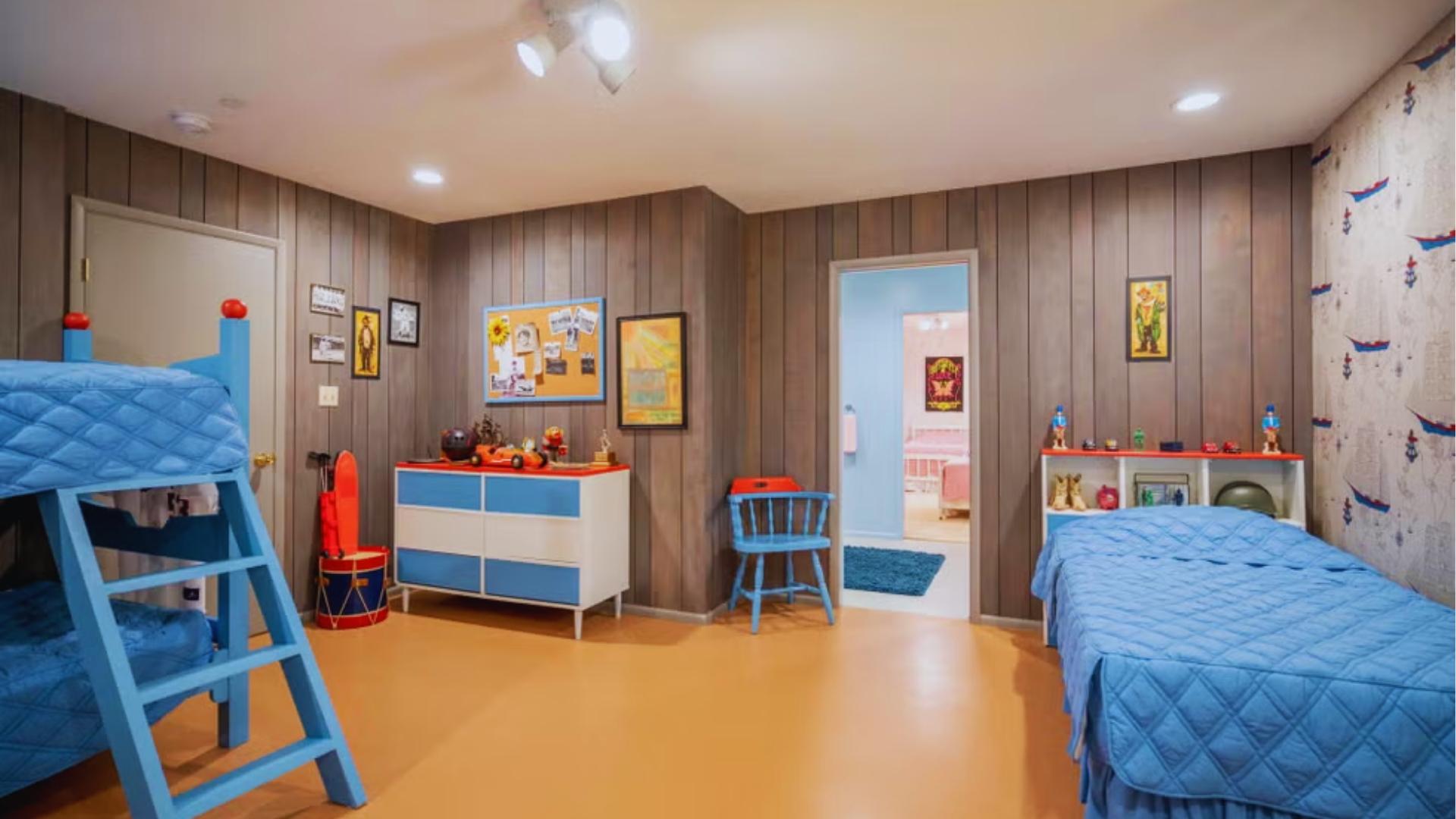 Brady boys’ bedroom with blue bunk beds, wood panel walls, and mid-century dresser and toys.