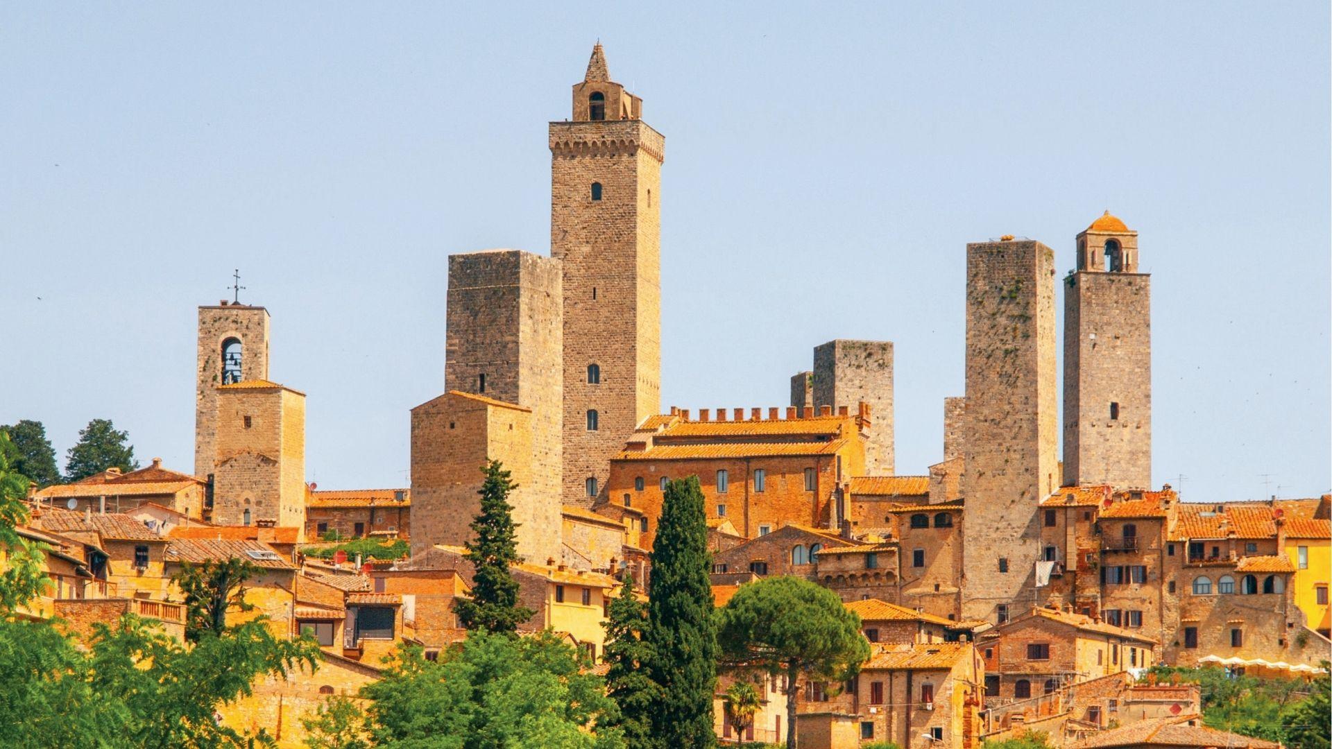Iconic medieval towers of San Gimignano reach into a clear blue sky, known as the “Town of Fine Towers”.