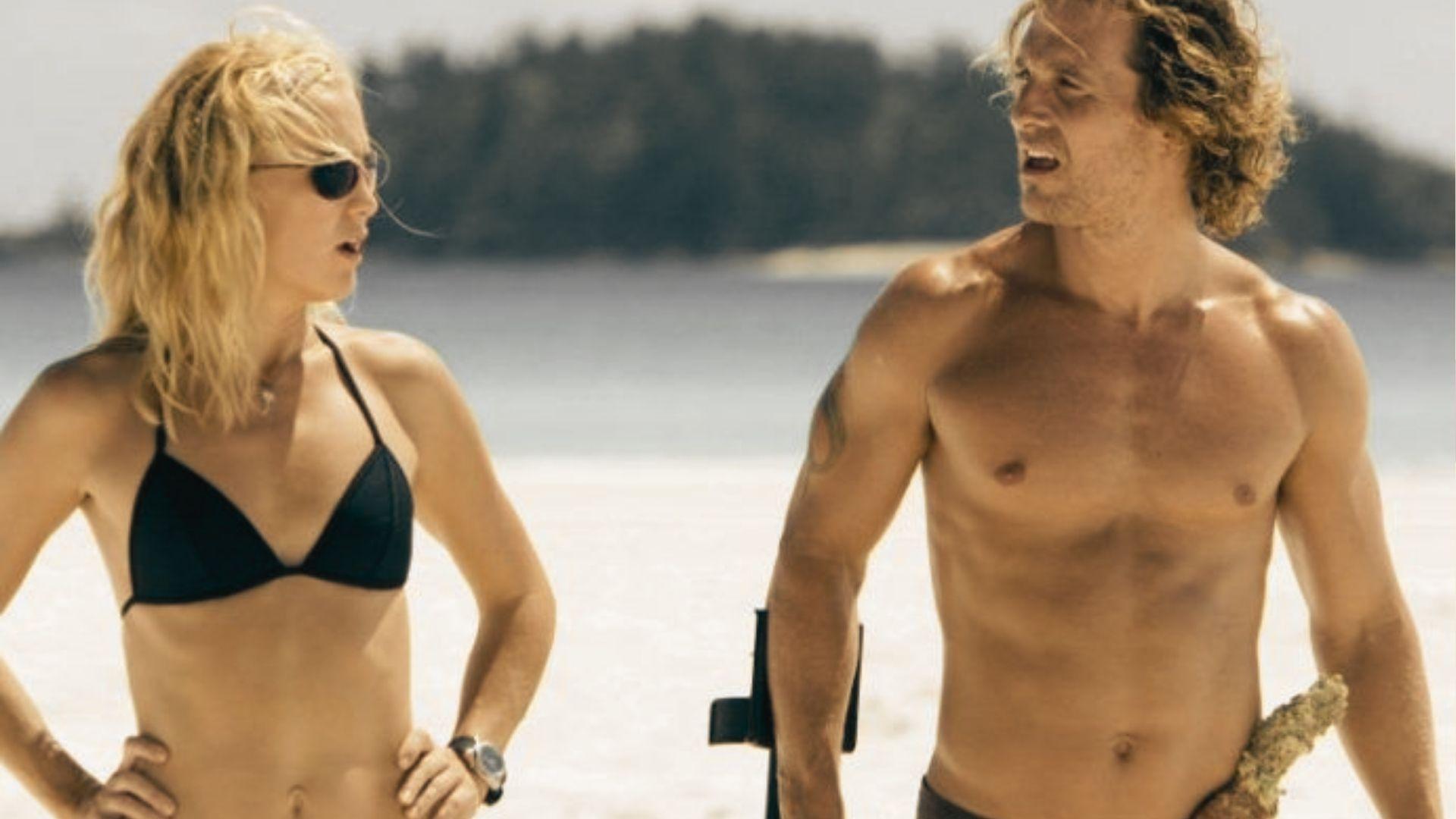 Tess and Ben argue on a sunlit beach, with calm ocean and distant trees behind them.
