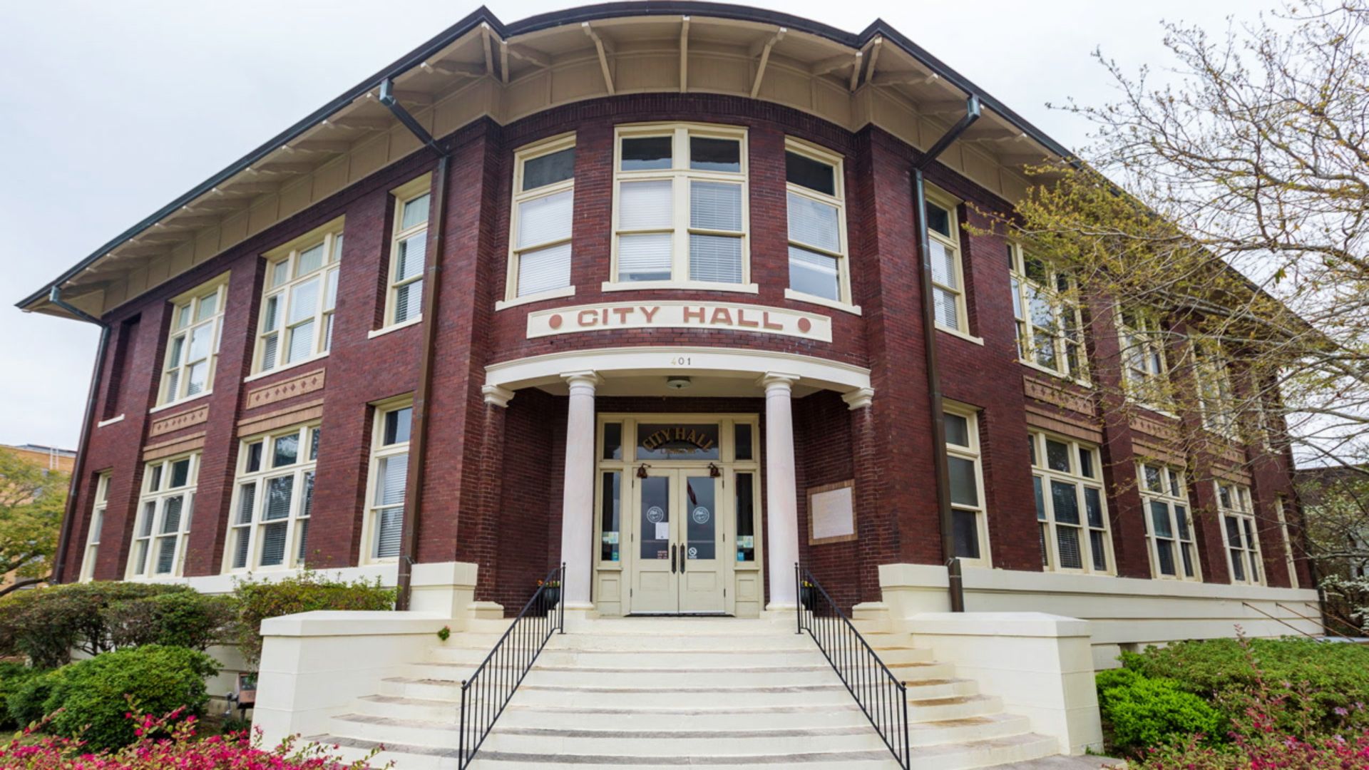 Historic red-brick City Hall in downtown Laurel, Mississippi with white columns and a central staircase.