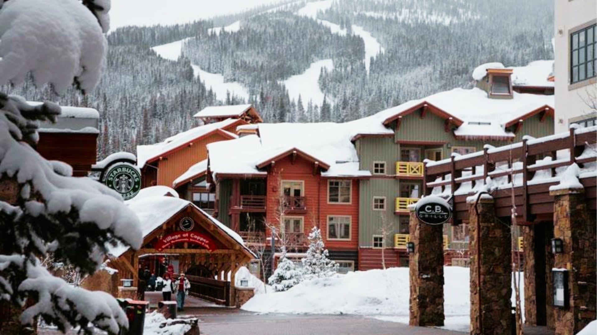 Snow covered mountain village street with colorful buildings, Starbucks sign, and skiers walking nearby
