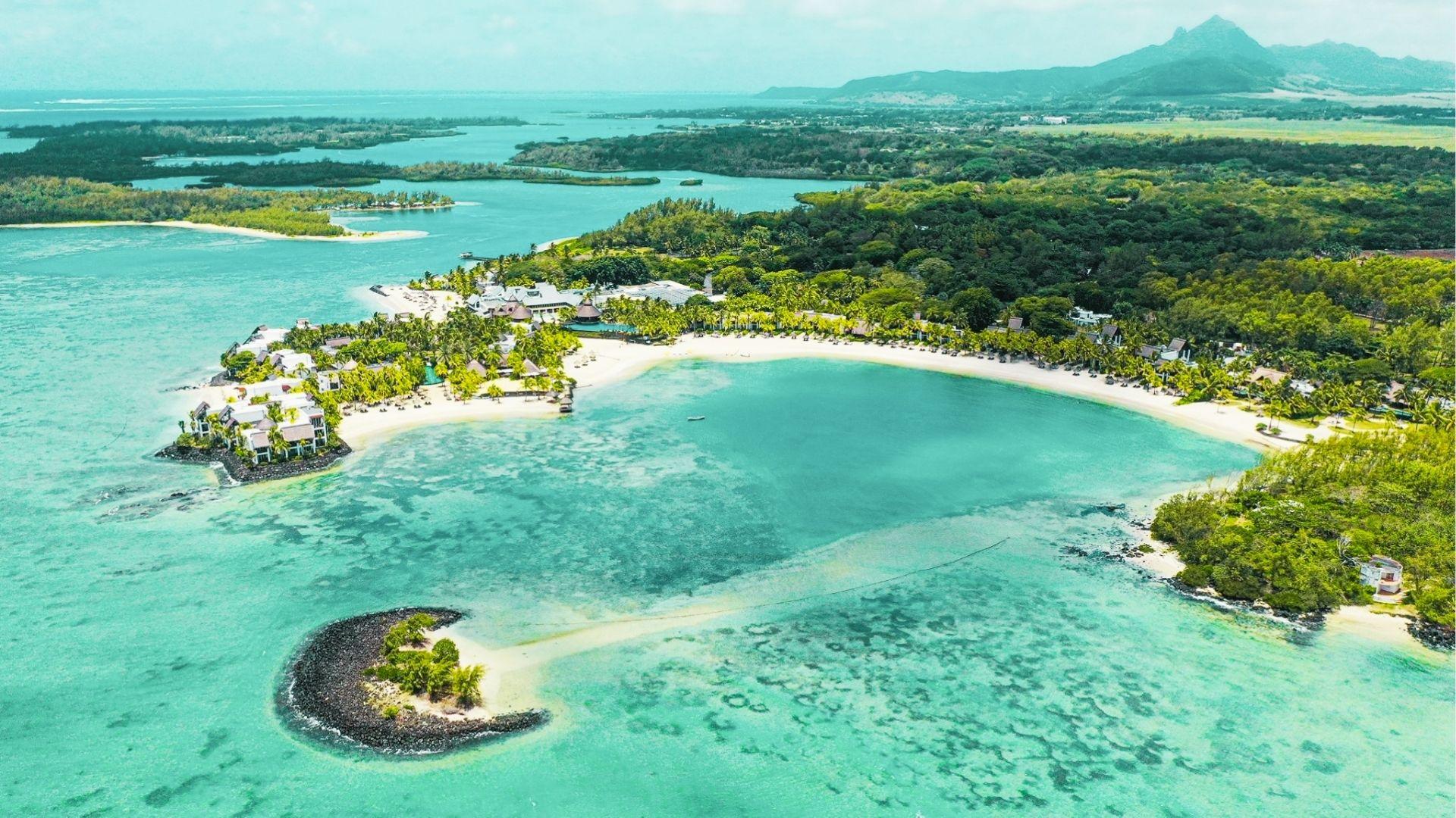 Aerial view of tropical resort on curved white sand beach with turquoise lagoon and mountains