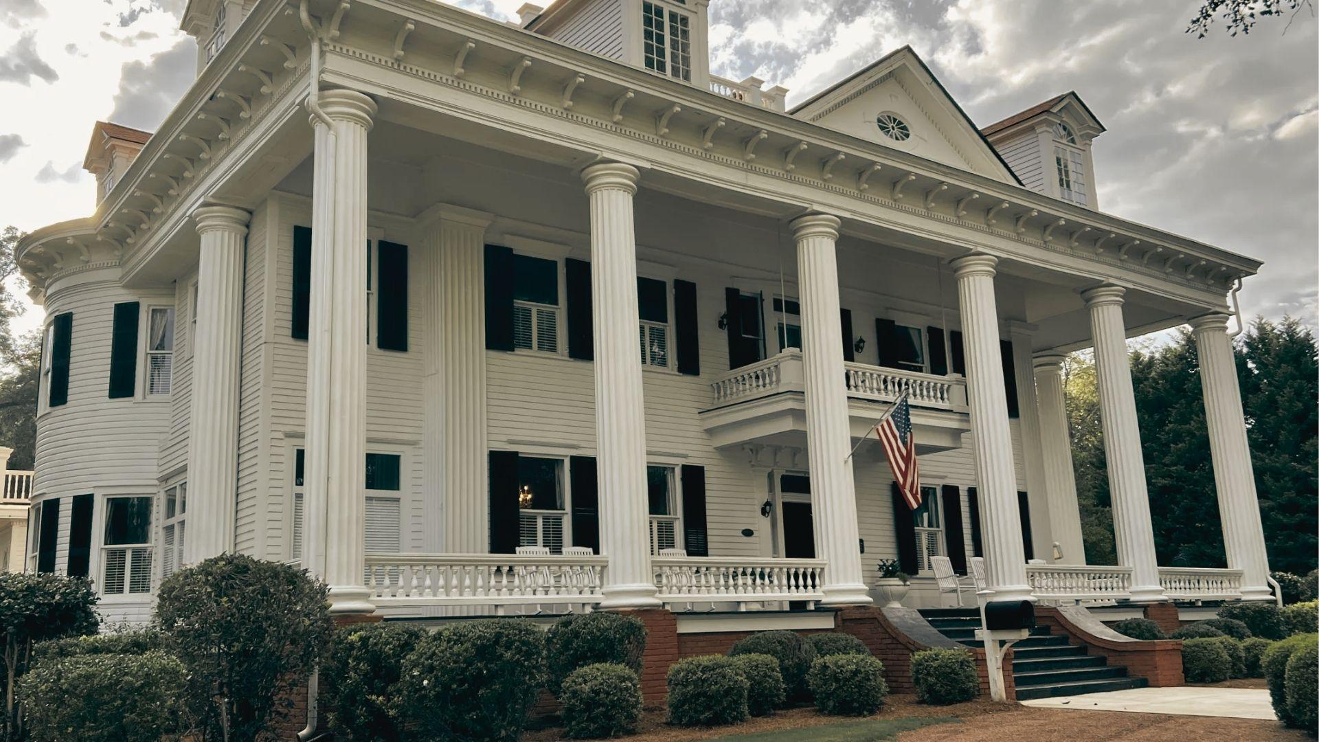 A grand white antebellum mansion with tall columns and an American flag on the porch.