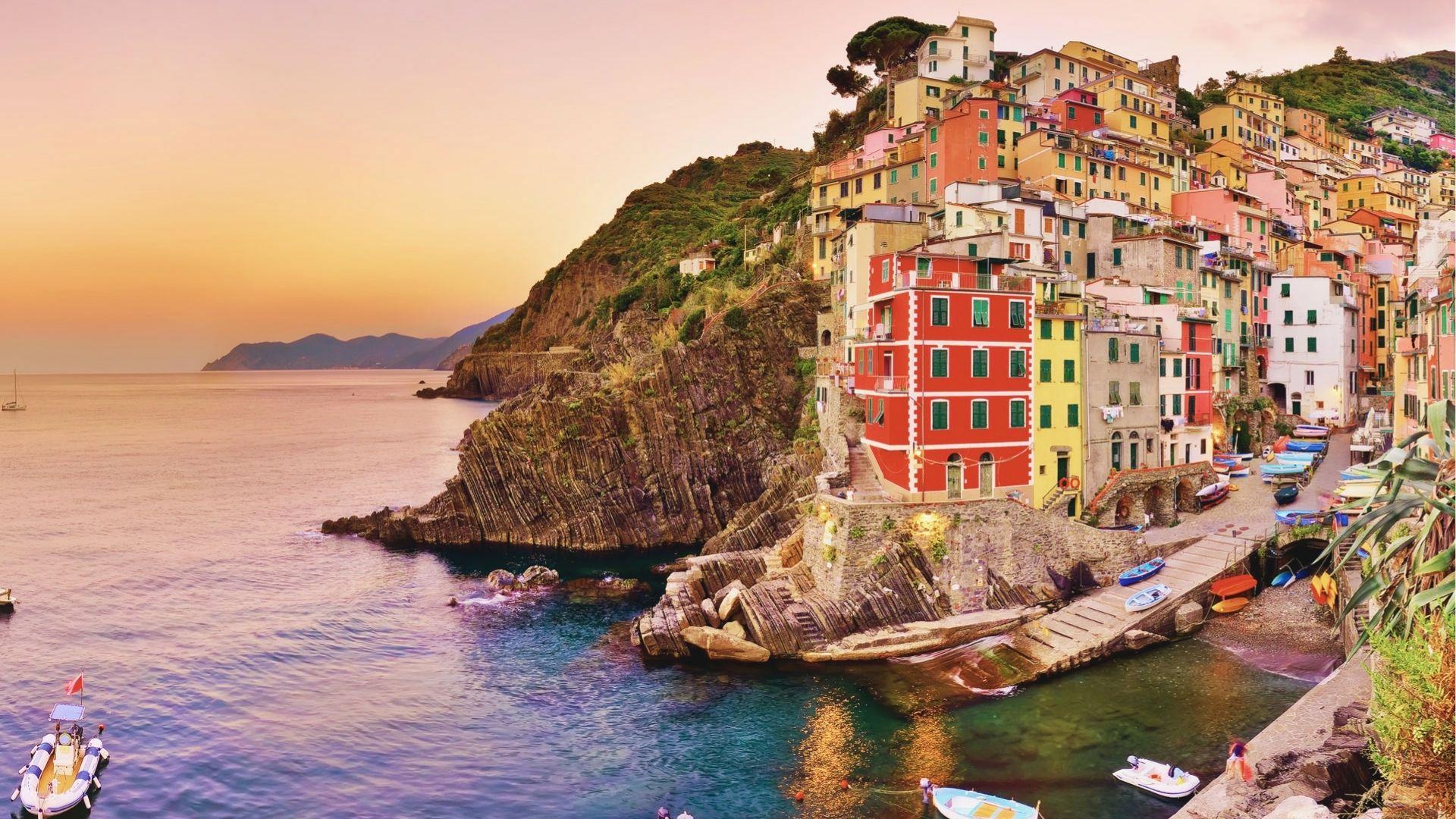Sunset paints the sky orange over Riomaggiore, Cinque Terre, with stacked pastel houses clinging to cliffs.