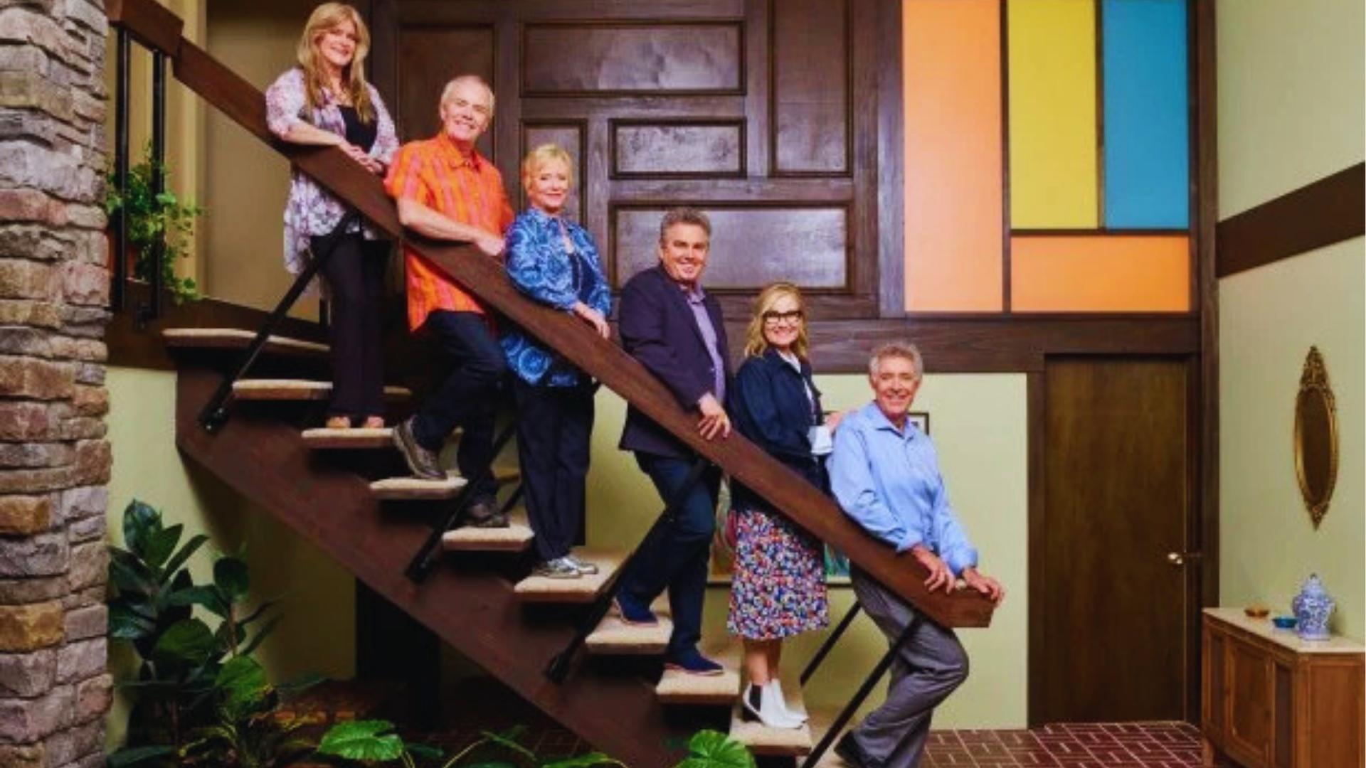 Brady Bunch cast on iconic floating staircase with colorful stained-glass panels and brick entry steps.