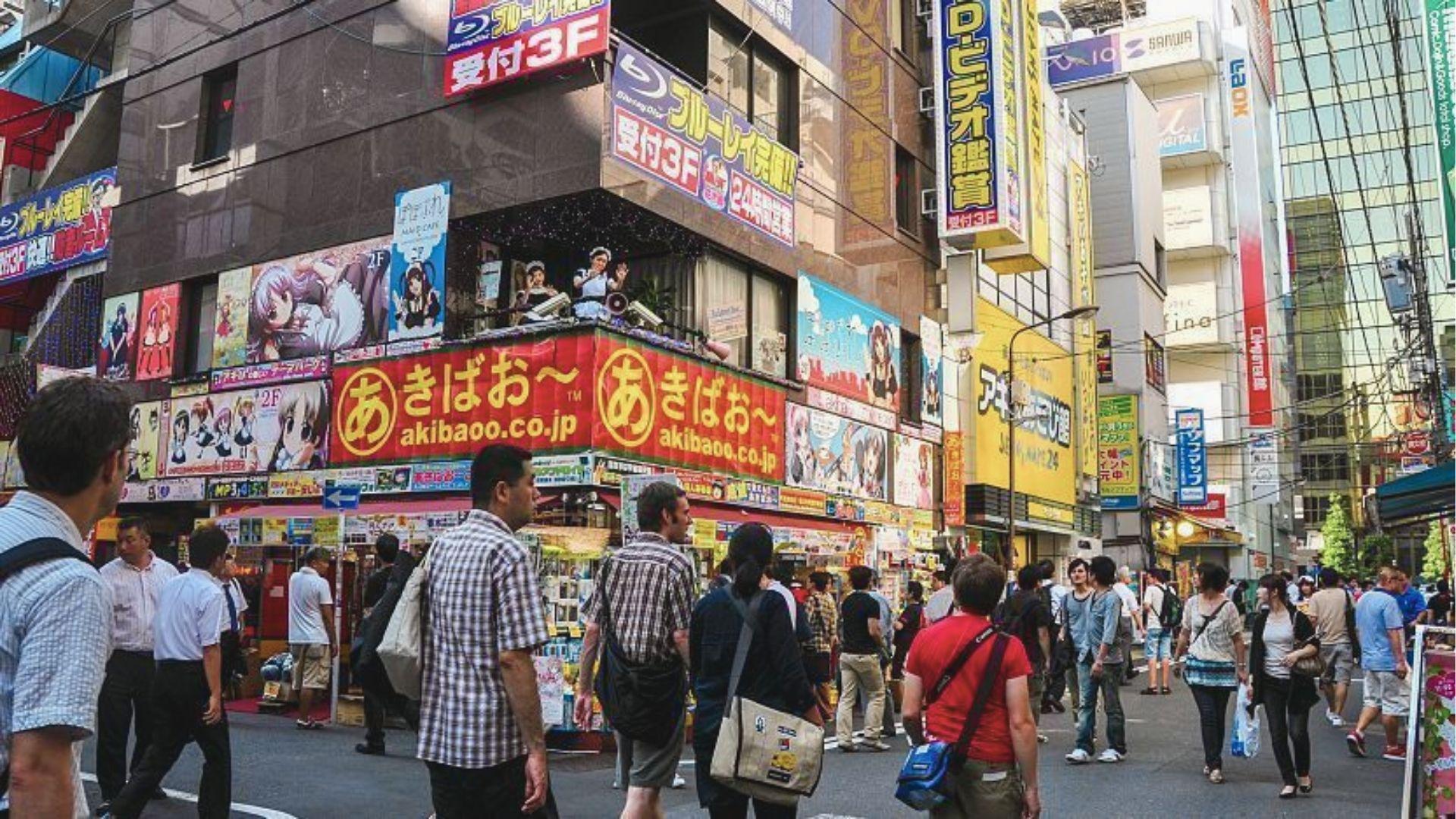 Crowded street in Akihabara lined with anime shops, electronics stores, and maid cafes under bright billboards.