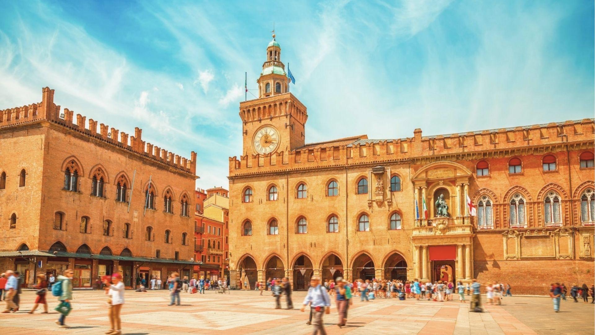 Piazza Maggiore in Bologna bustles with people beneath the medieval Palazzo d’Accursio and its clock tower.