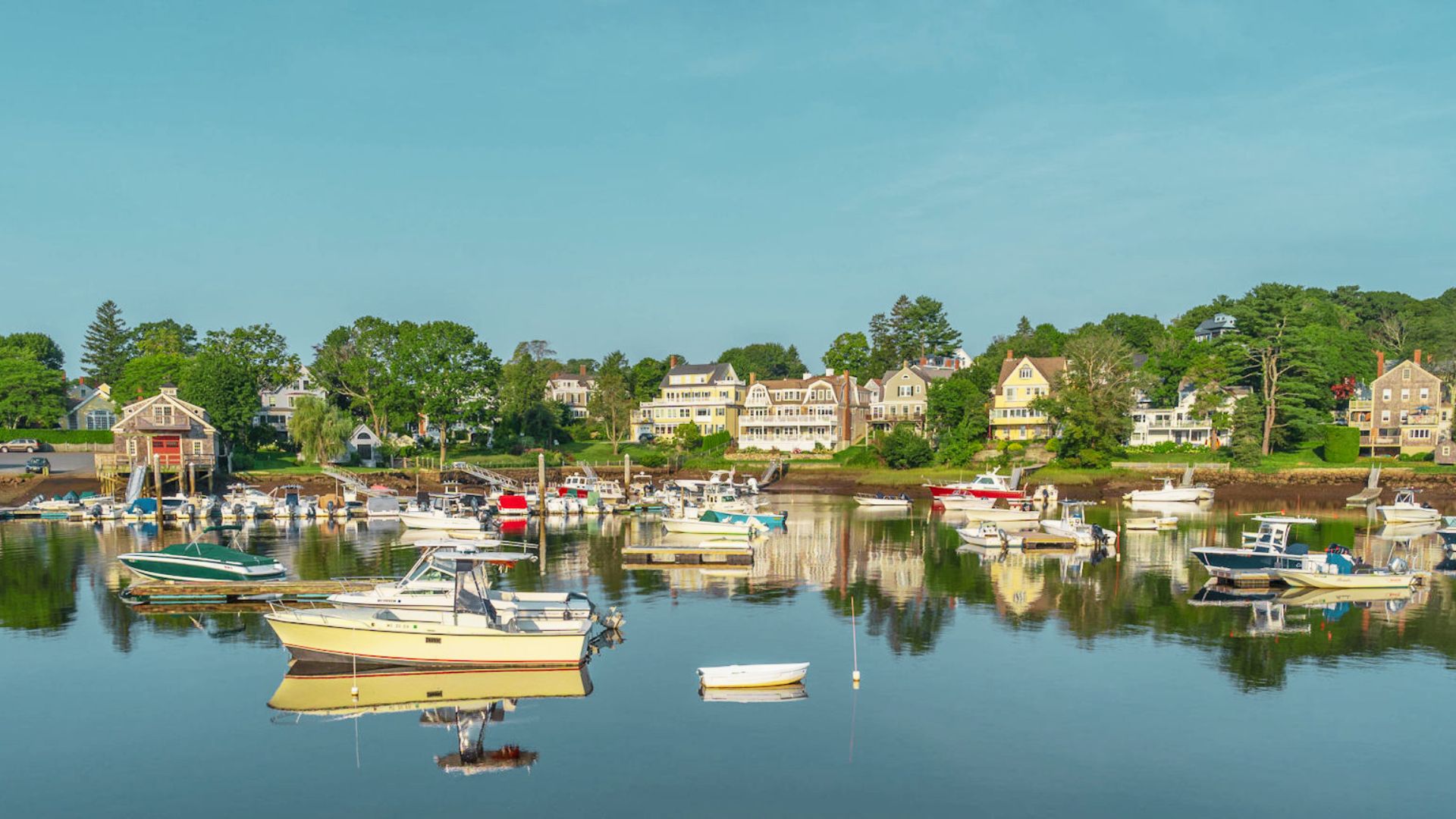 Boats and yachts reflect in the still waters of Manchester Harbor, with historic waterfront homes lining the shore.