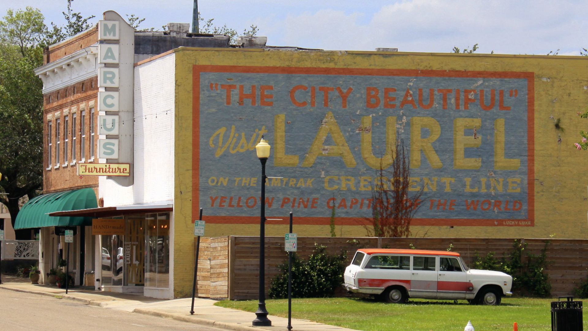 Iconic yellow mural reading "The City Beautiful Visit LAUREL" on a downtown building beside Marcus Furniture.