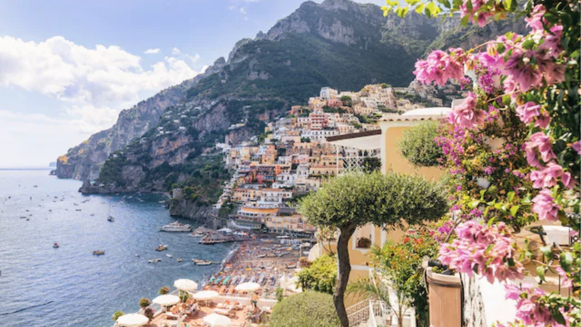 Sunlit pastel houses cascade down steep cliffs toward the Tyrrhenian Sea in Positano, Amalfi Coast. 