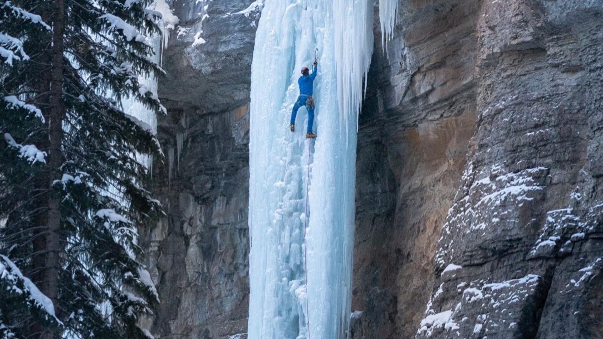 A MAN ICE CLIMBING ON FROZEN WATERFALLS