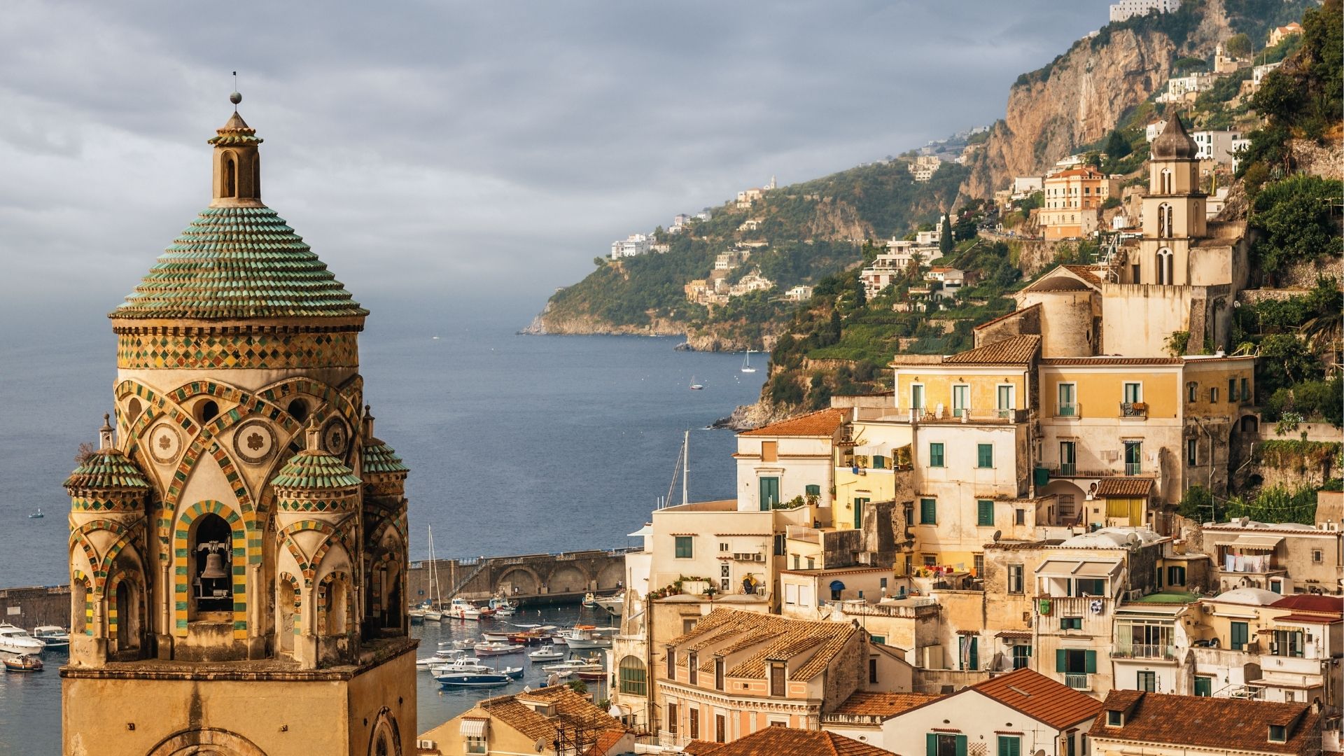 The ornate majolica-tiled dome of Amalfi Cathedral stands out among terracotta rooftops and stone buildings. 
