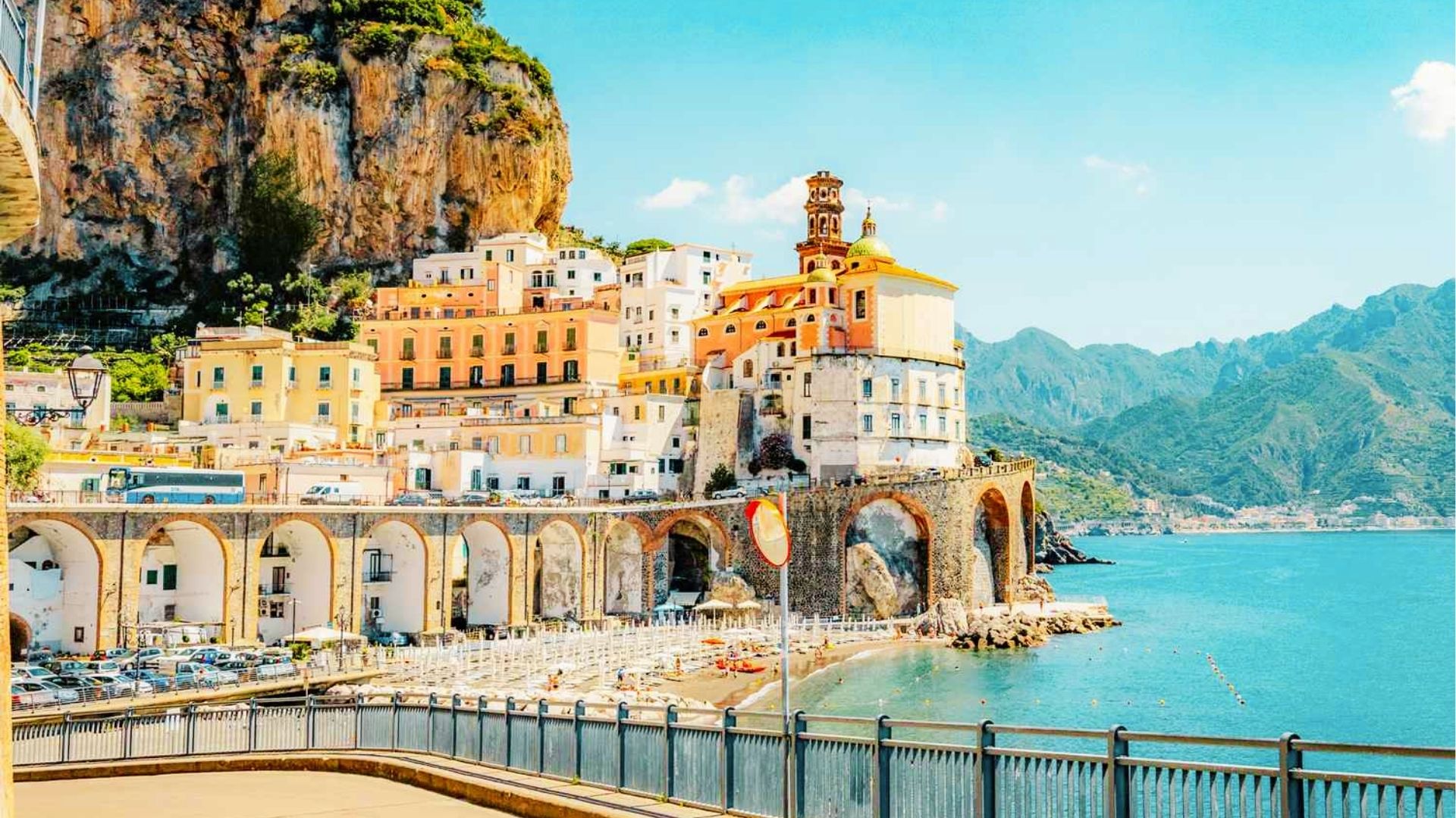 The town of Atrani sits beneath dramatic cliffs, with its yellow church and arched viaduct facing the sea. 