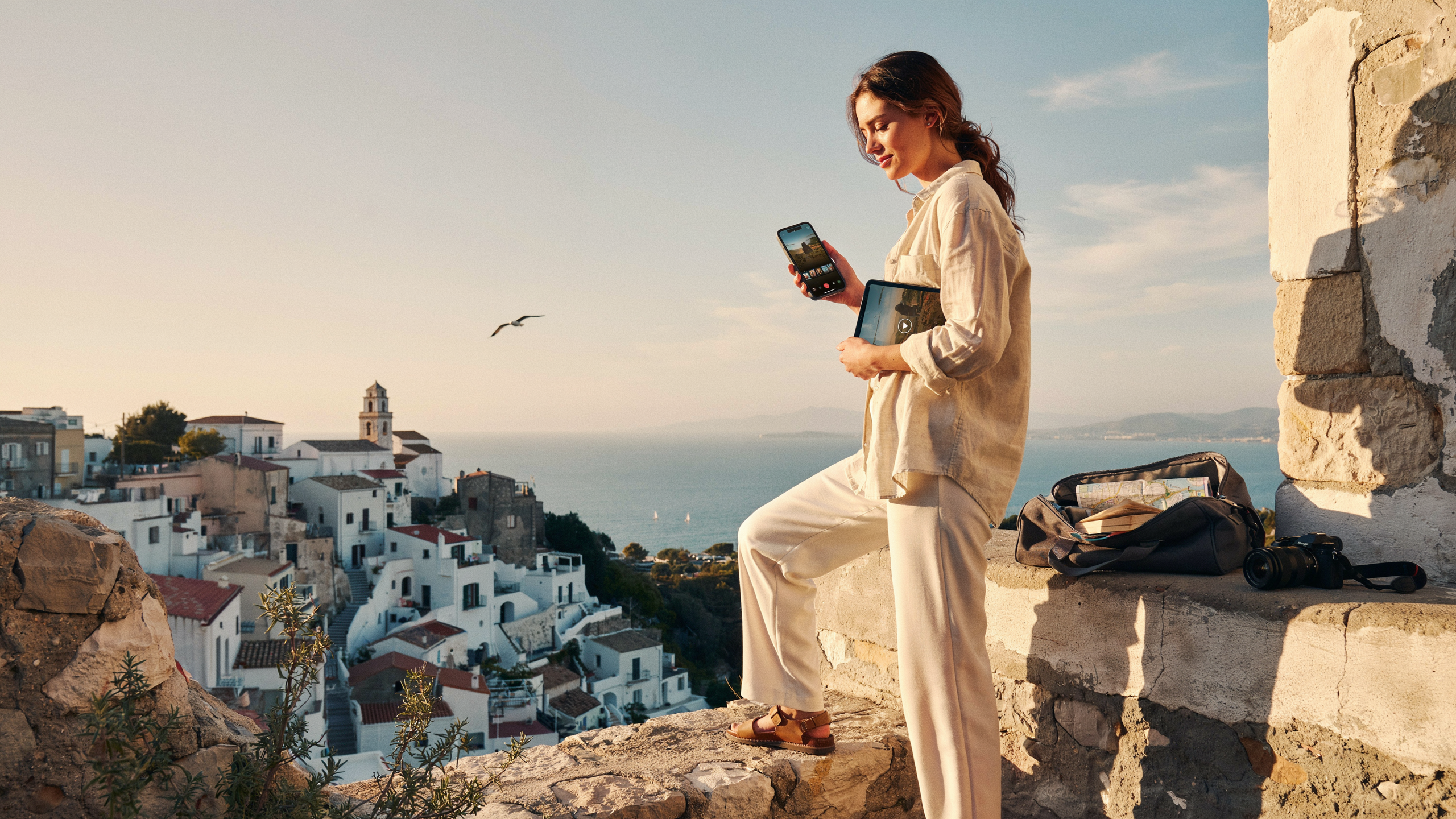 A woman dressed in white stands on a ledge, overlooking the ocean with a serene expression.