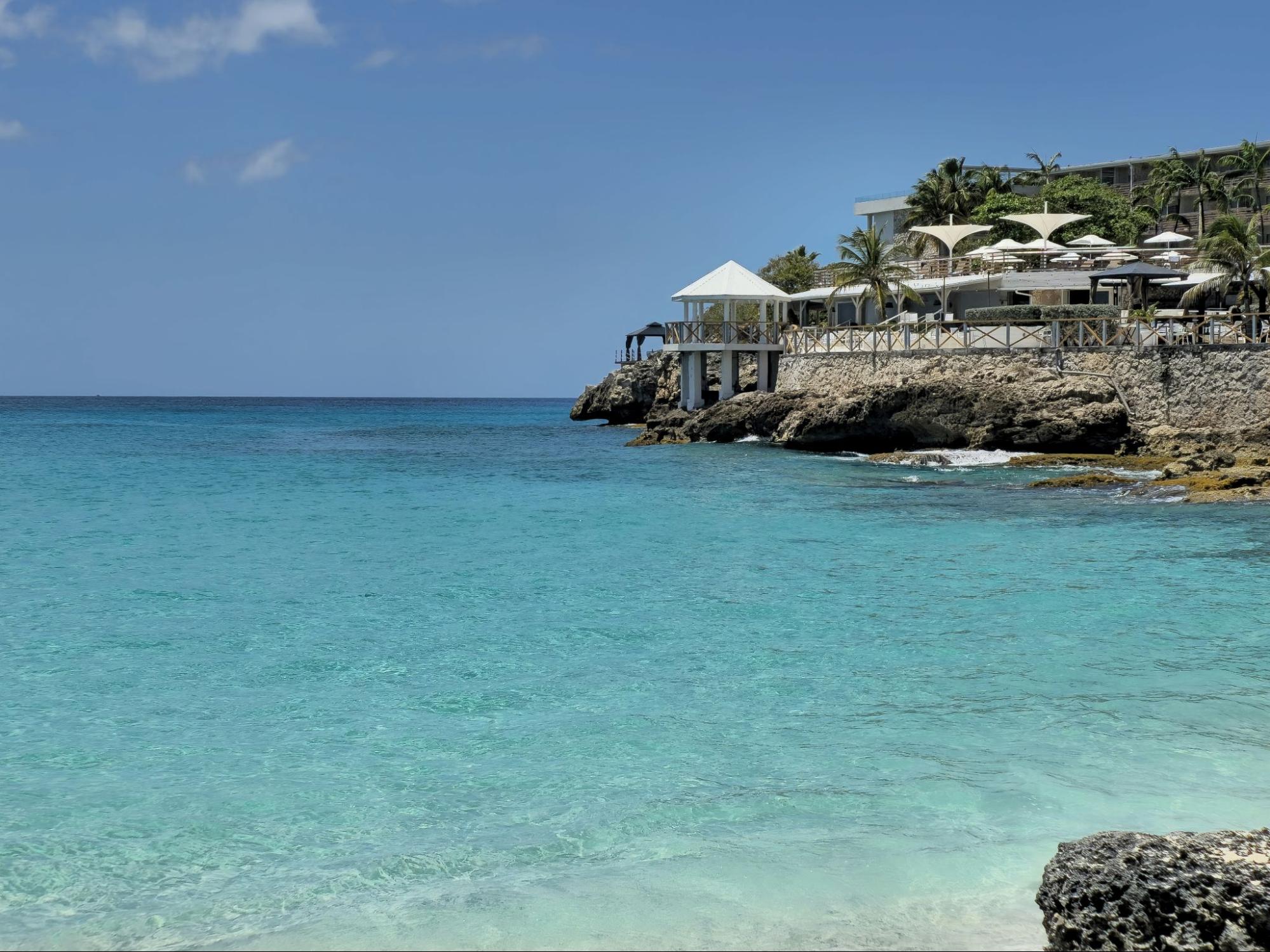 A scenic beach view featuring a hotel situated along the shoreline, with gentle waves lapping at the sand.