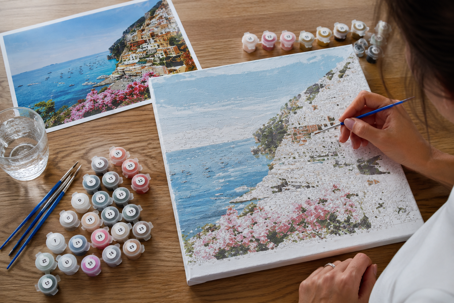 A woman paints a vibrant scene featuring the sea and colorful flowers on a canvas outdoors.
