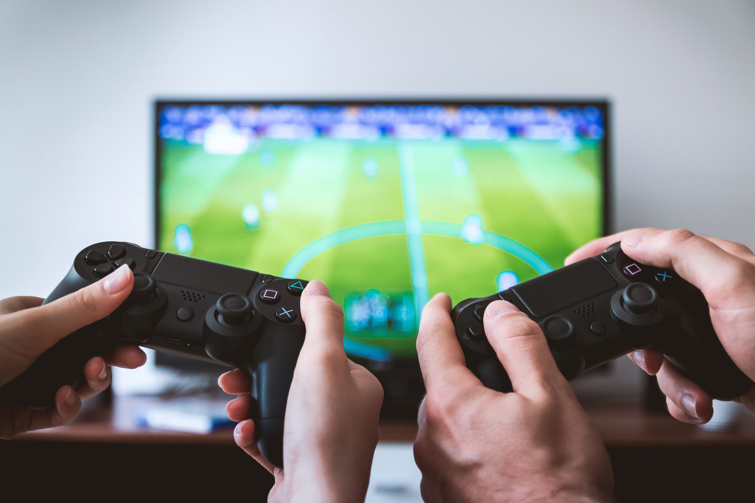 Two individuals sit on a couch, each holding a video game controller, focused on a television screen in front of them.