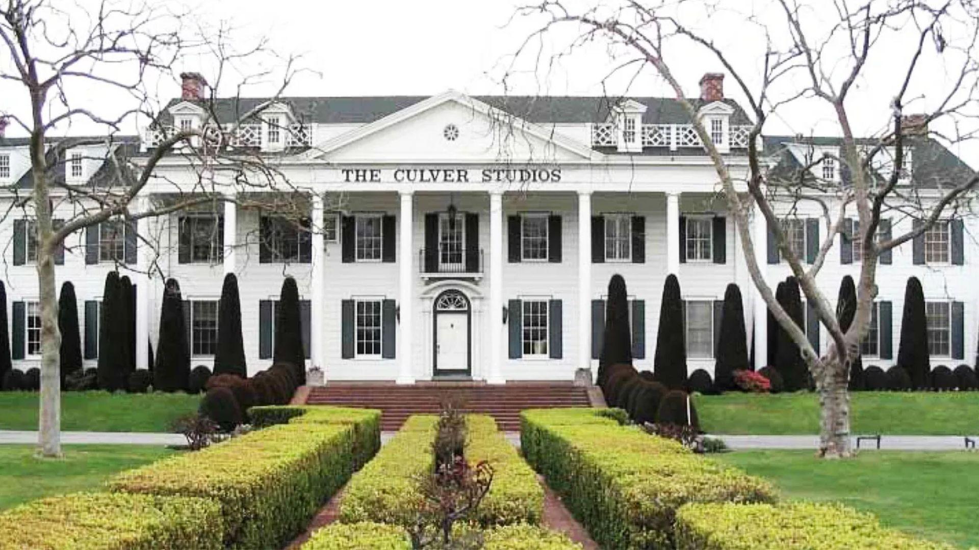 The white neoclassical facade of The Culver Studios in Los Angeles behind a formal hedge garden.