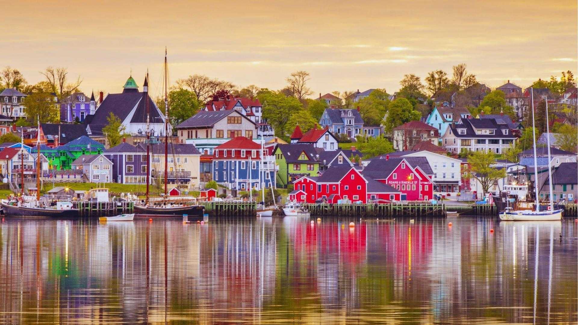 Colorful waterfront buildings reflected in Lunenburg harbor at sunset, Nova Scotia location for We Were Liars.