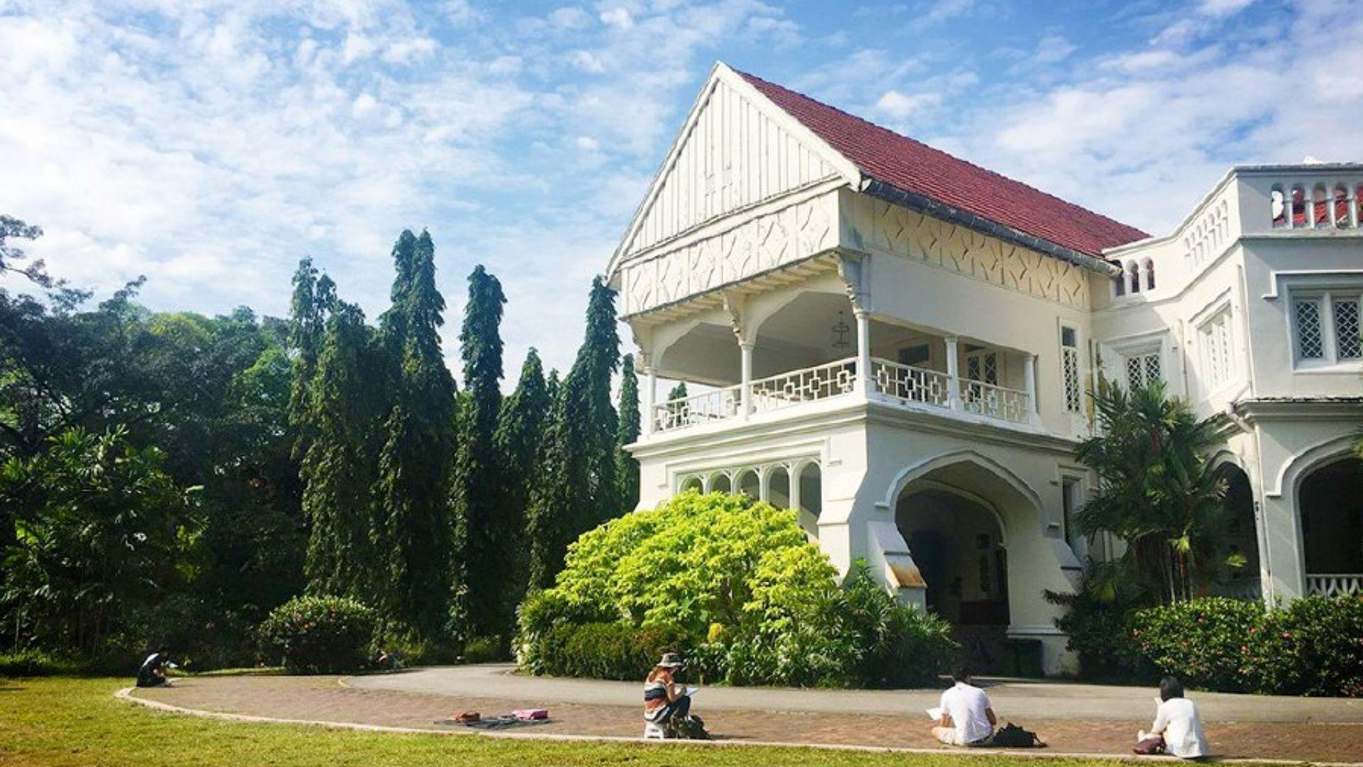 White luxury mansion in Malaysia featuring people sitting outside in the sun.