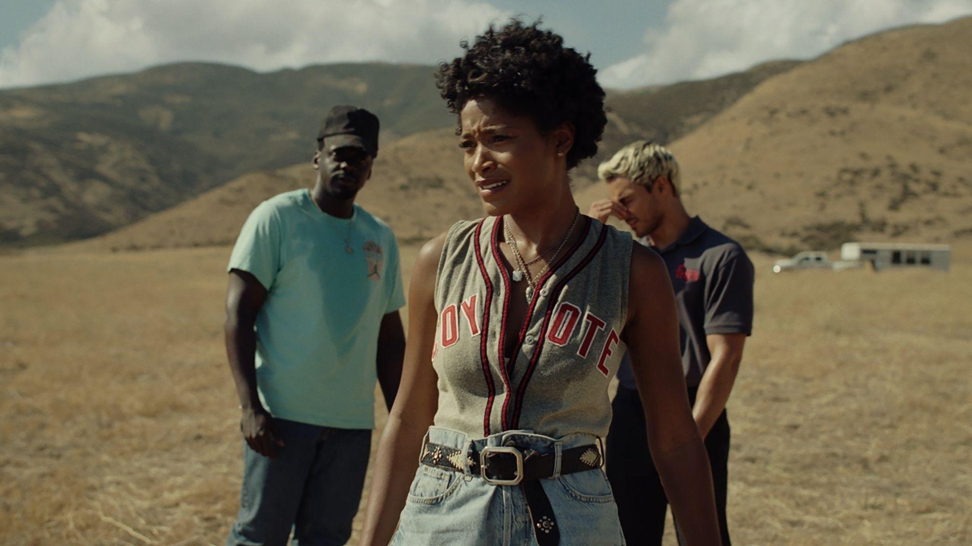 Still from NOPE. Em reacts in distress in dry field, OJ and Angel stand behind her under brown hills.