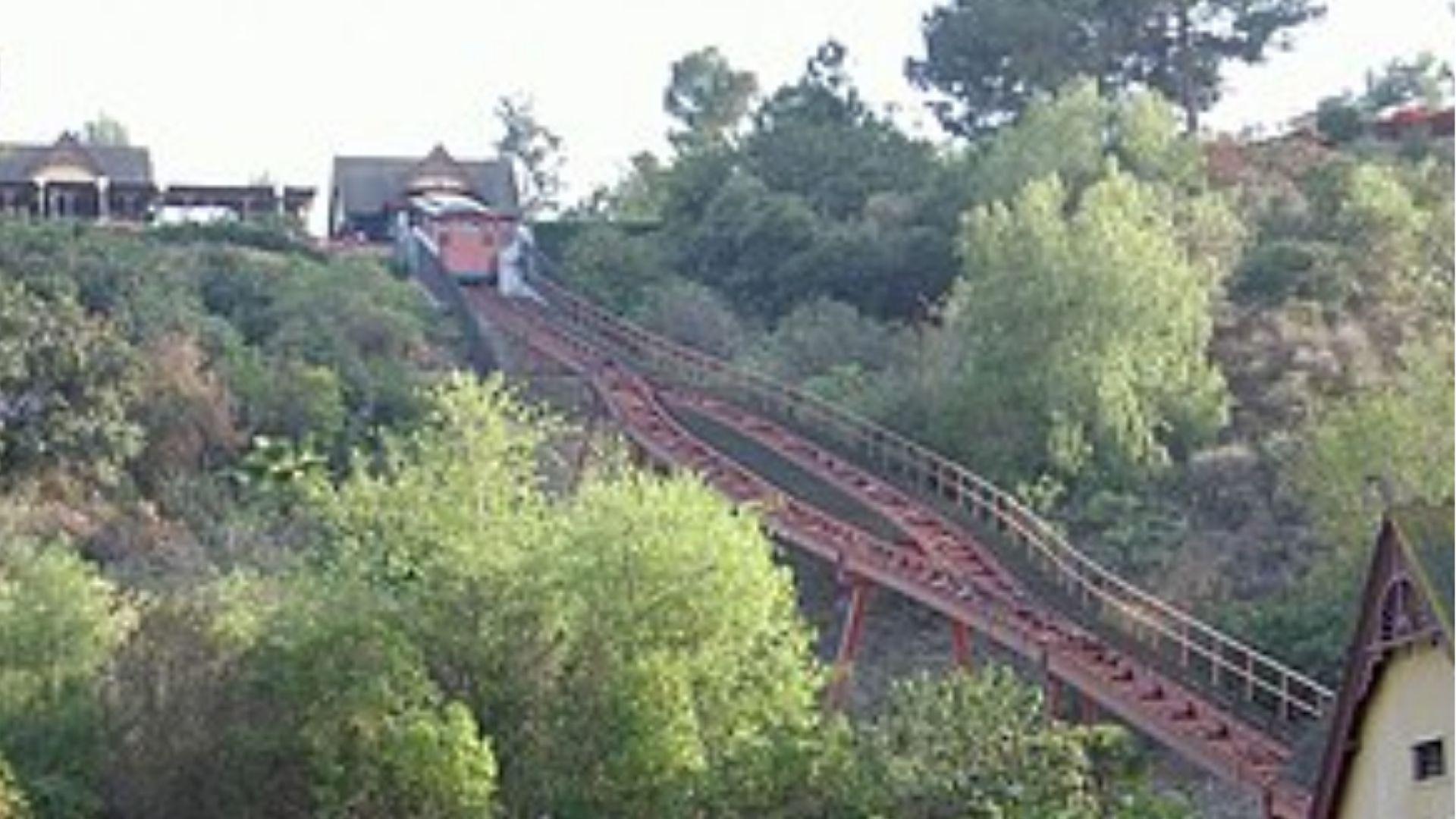A funicular railway car climbs a steep wooded hillside between two stations in California.