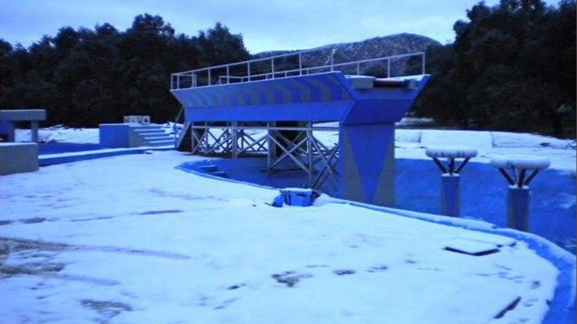 Blue Wipeout obstacle platform covered in snow with trees and hills in background