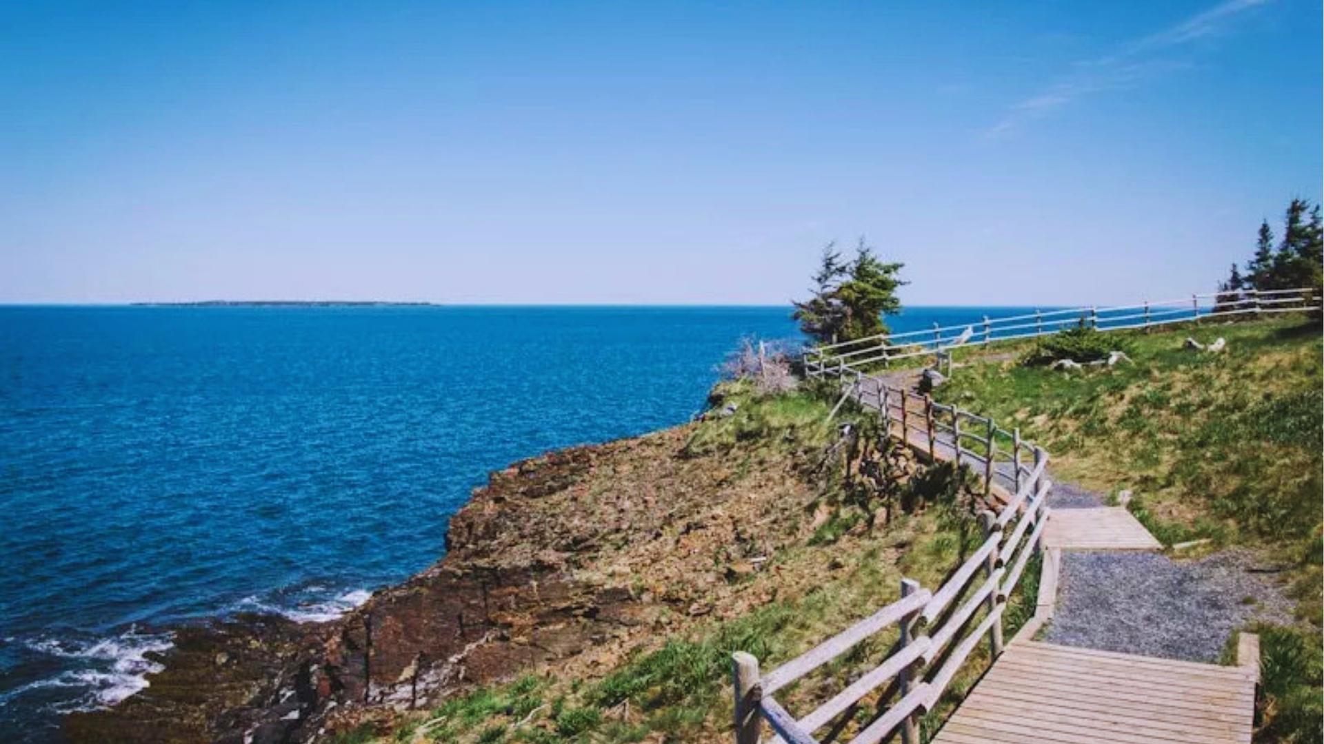 Wooden boardwalk along rocky Nova Scotia coastline with blue ocean, used for We Were Liars walking scenes.