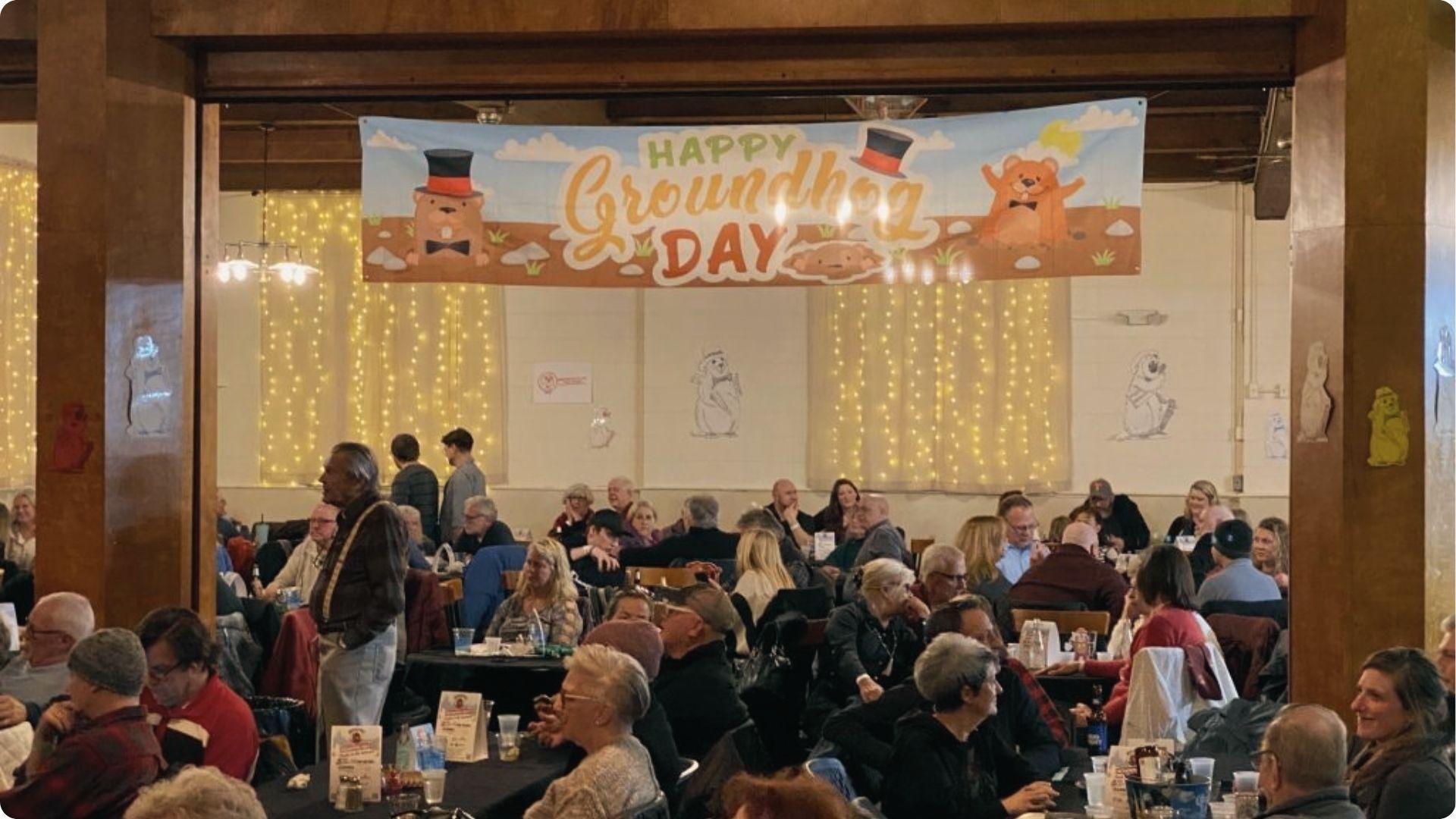 “Happy Groundhog Day” banner over crowd at Moose Lodge. Woodstock’s real festival hall scene.