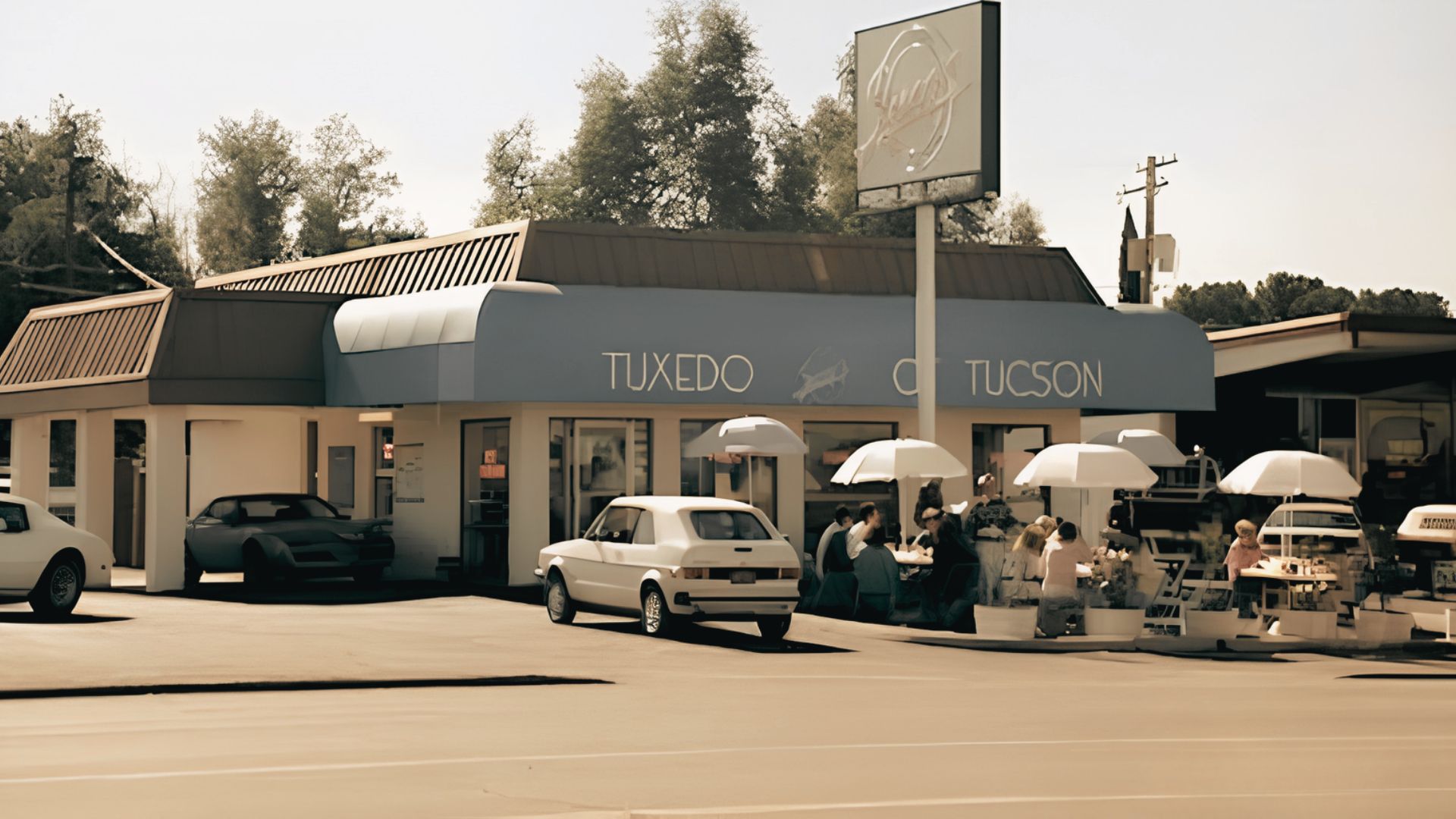 Daytime shot of a 1980s-style restaurant with “TUXEDO TUCSON” signage and outdoor umbrella seating.